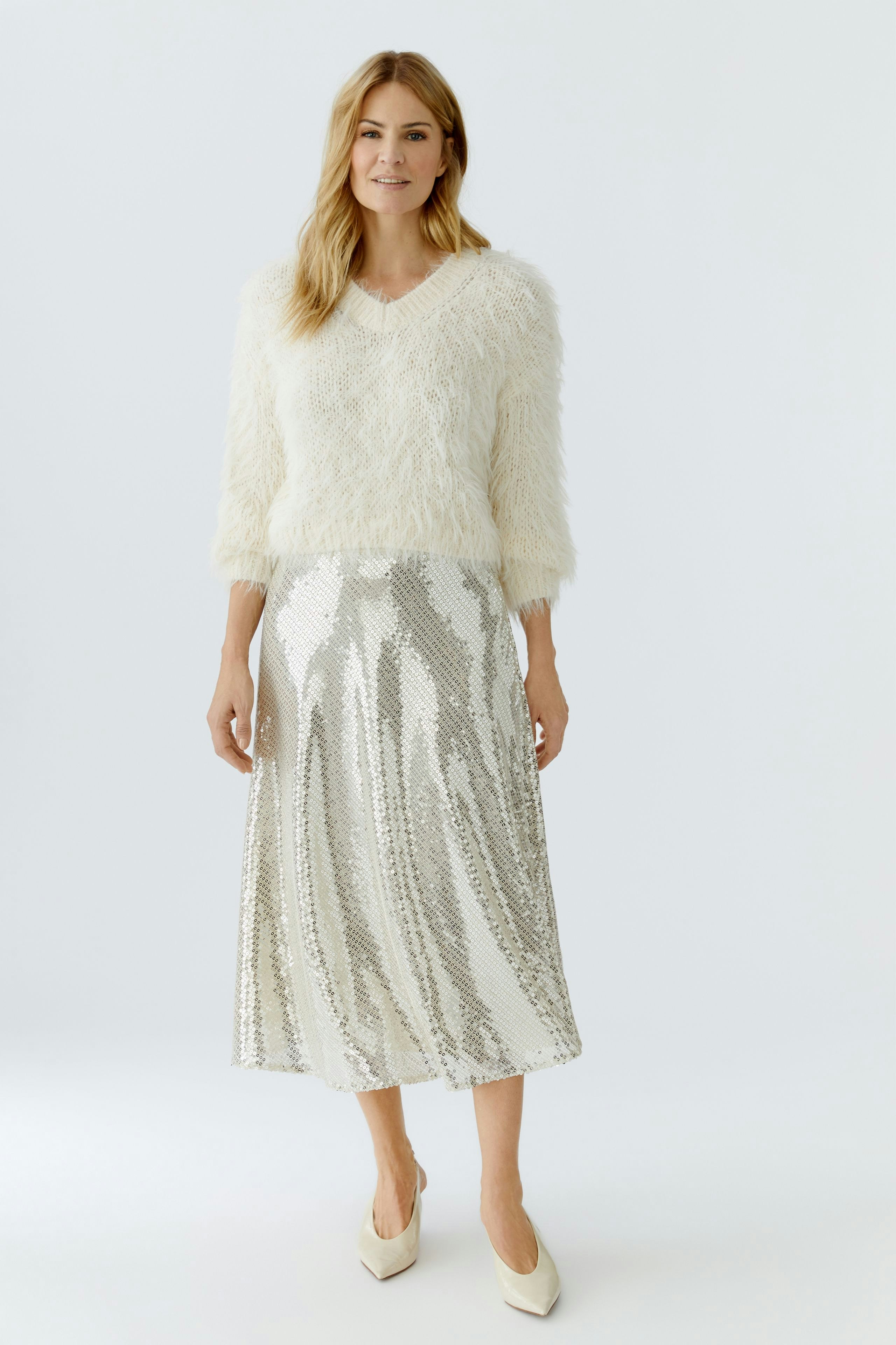 Cozy women's pullover: A woman in a fluffy white pullover paired with a shiny silver skirt.