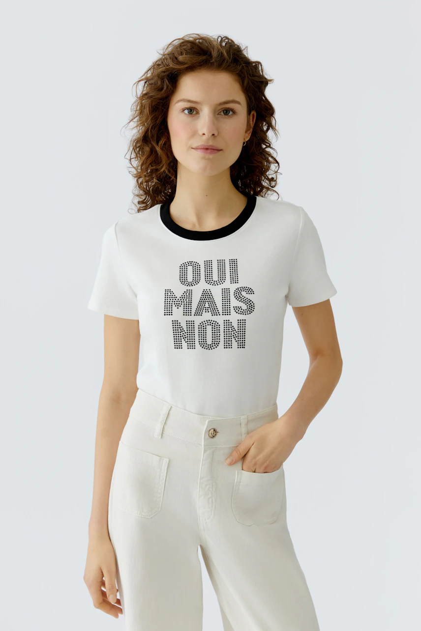 Casual women's T-shirt: Young woman in a white tee with black lettering, paired with light pants.