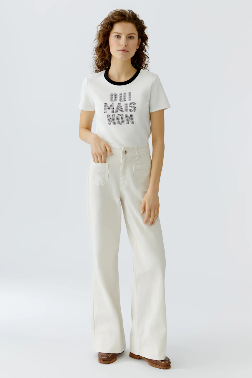 Casual women's T-shirt: Young woman in a white tee with bold text, paired with light pants.
