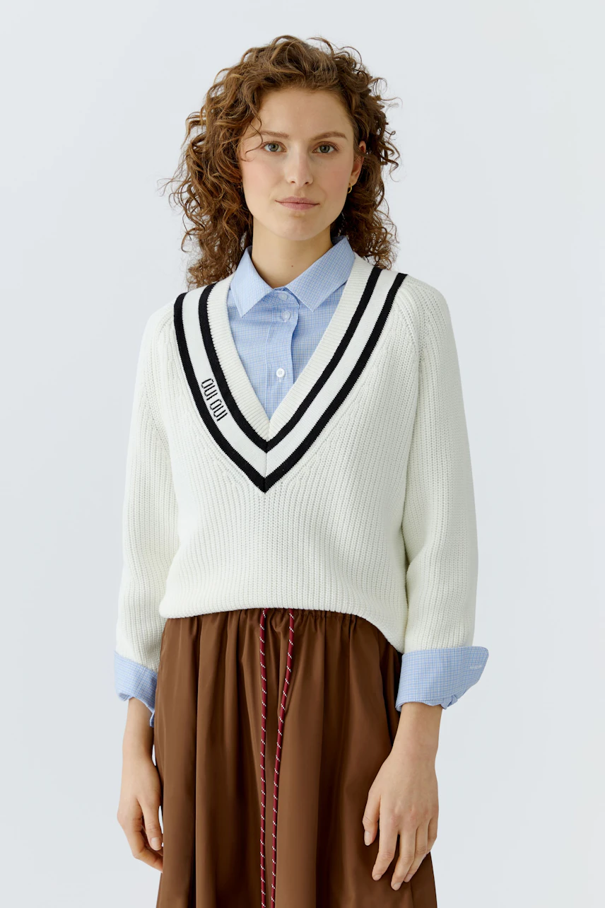 Casual women's pullover: A woman in a white ribbed pullover with a V-neck and sporty stripes.