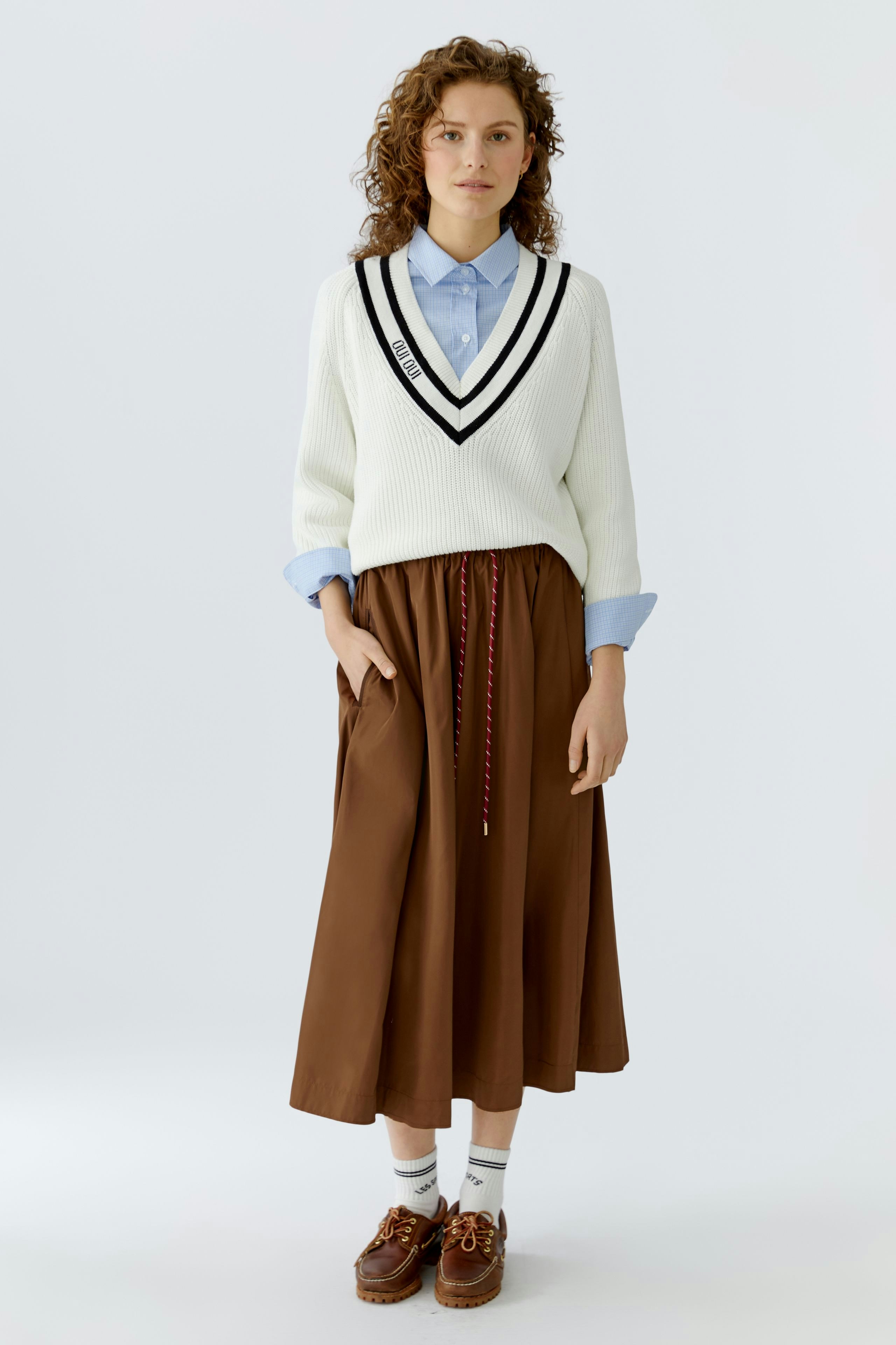Casual women's pullover: A woman in a white pullover with a V-neck and black stripes, paired with a brown skirt.