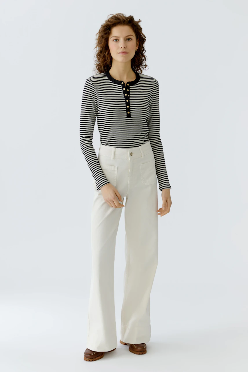 Striped long-sleeve shirt: Woman in a black and white striped pullover with buttons and wide white pants.