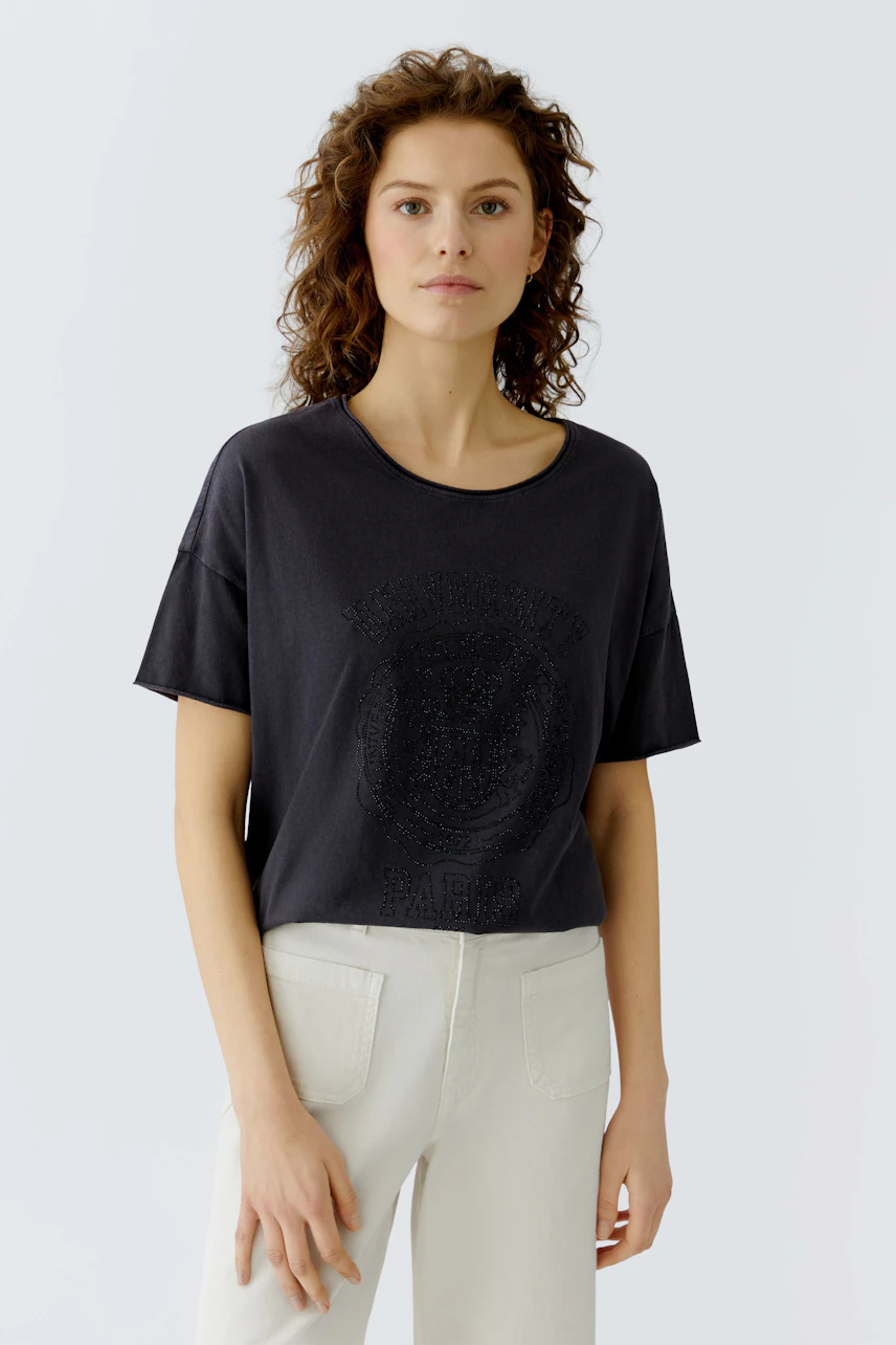 Casual women's T-shirt: Young woman in a black tee with a graphic print, paired with light pants.