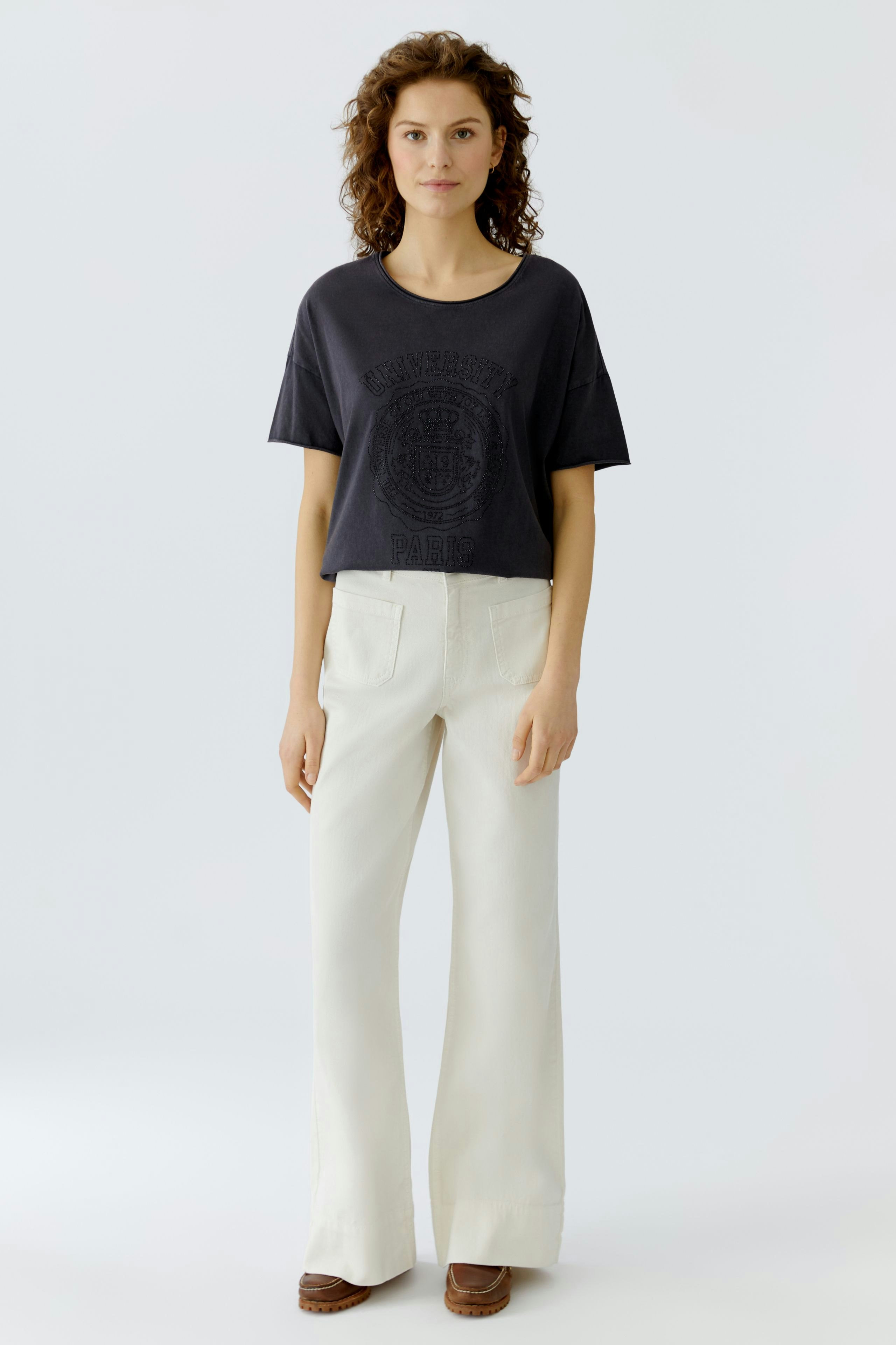 Casual women's T-shirt: Young woman in a dark tee with a graphic print, paired with light trousers.