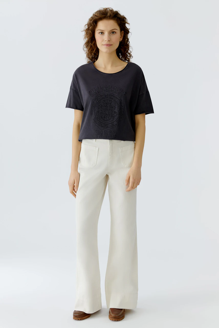 Casual women's T-shirt: Young woman in a dark tee with a graphic print, paired with light trousers.