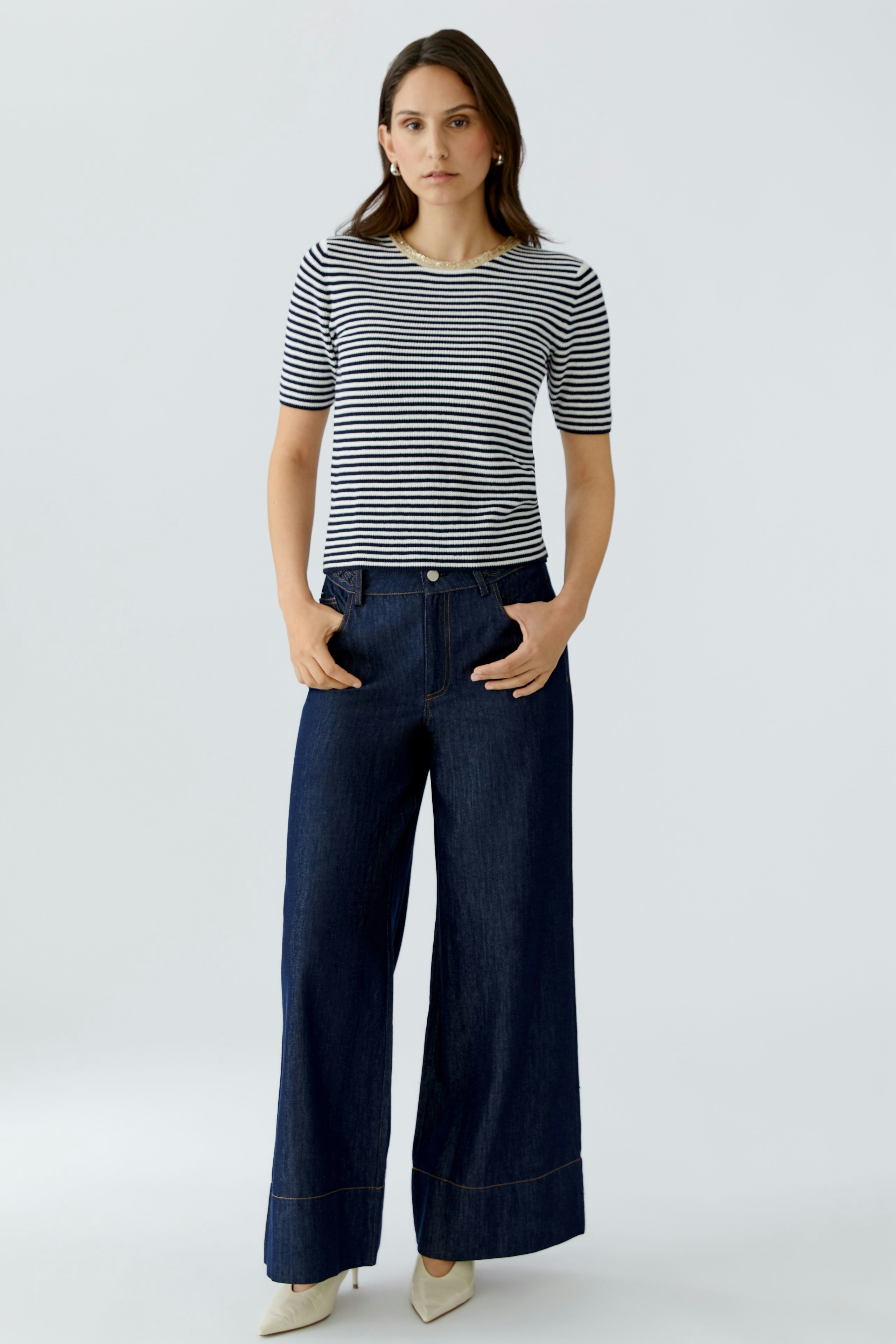 Casual women's pullover: Young woman in a striped pullover and wide-leg jeans stands confidently.