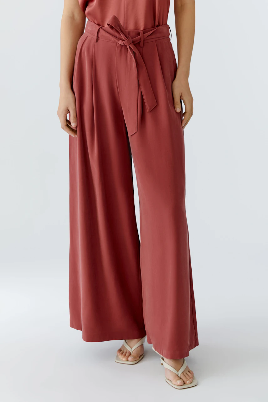 Wide-leg trousers: A woman in rust-colored, high-waisted trousers with a tie belt, showcasing a relaxed fit.