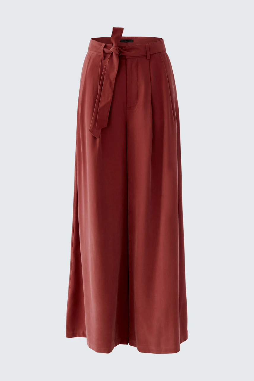 Wide-leg trousers: A woman in rust-colored pleated trousers with a tied waist, showcasing a relaxed style.