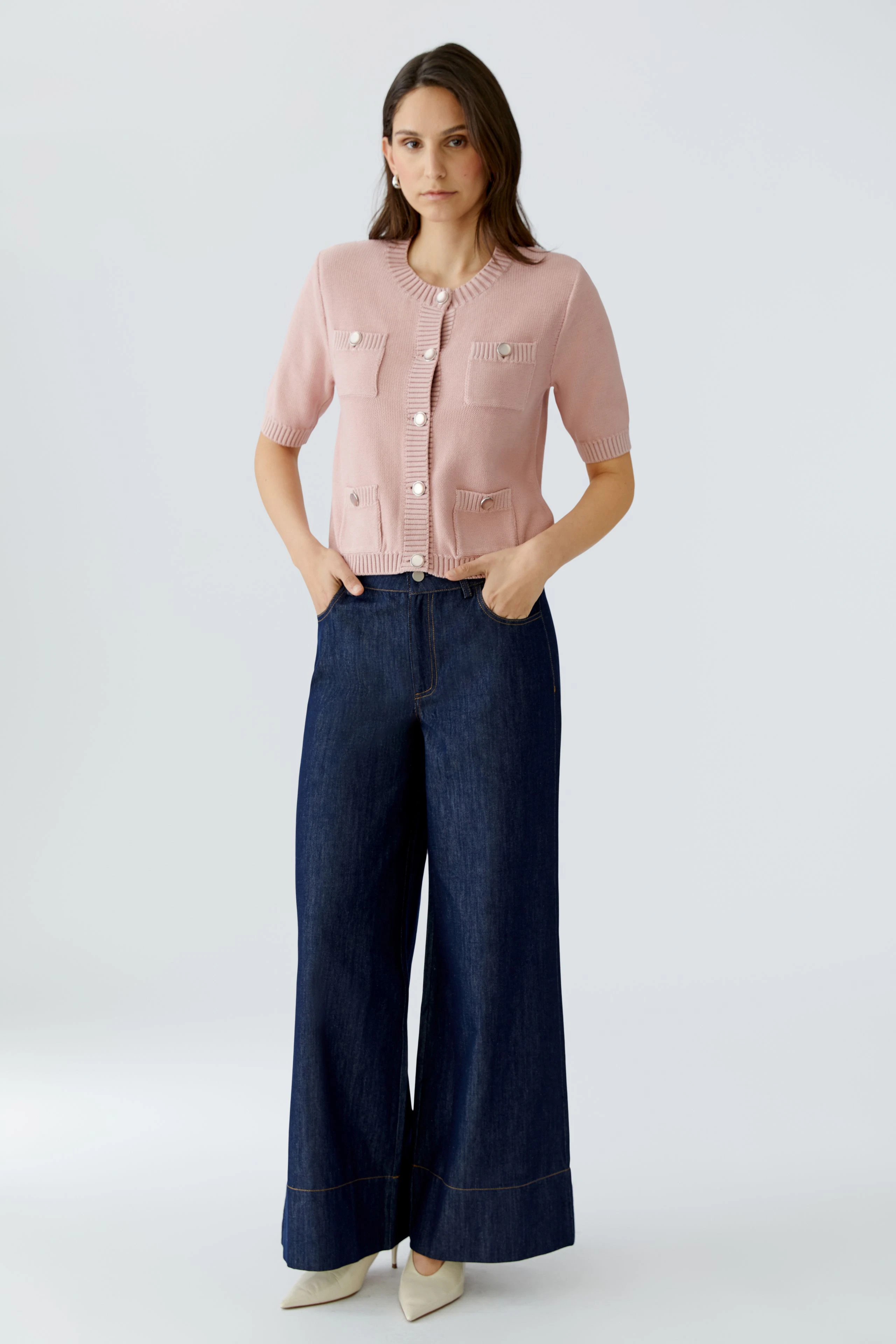 Damen-Strickjacke in zartem Rosa mit kurzen Ärmeln und Taschen, kombiniert mit weiten Jeans.