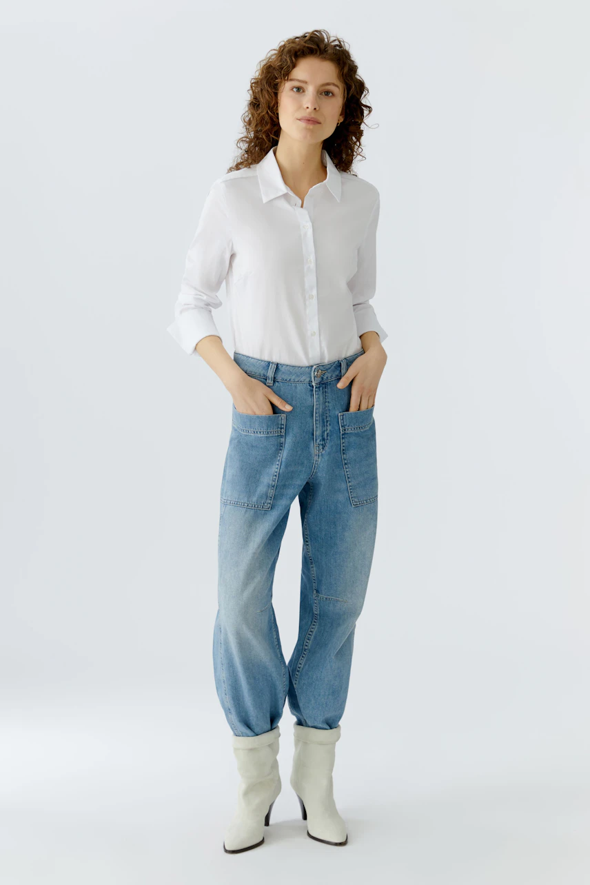 Bequeme Jeans Barrel: Frau in lässigen, hellblauen Jeans mit weitem Schnitt und weißen Bluse.