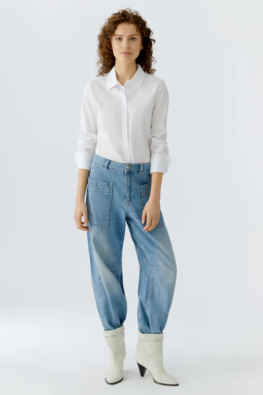 Bequeme Jeans Barrel: Junge Frau in lässigen, hellblauen Jeans mit weitem Schnitt und weißem Hemd.