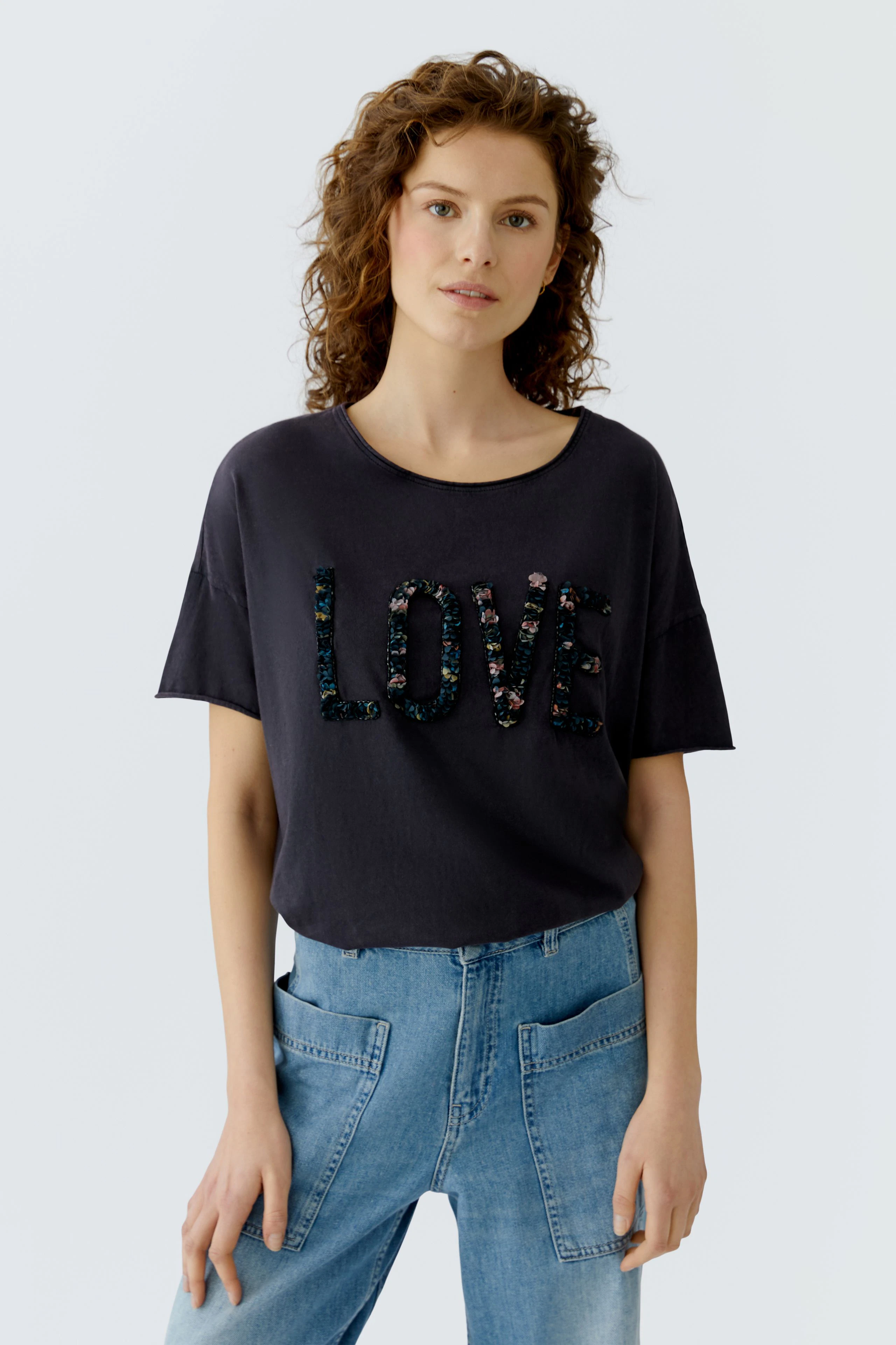 Casual women's T-shirt: Young woman in a dark tee with sequined 'LOVE' lettering and relaxed fit.