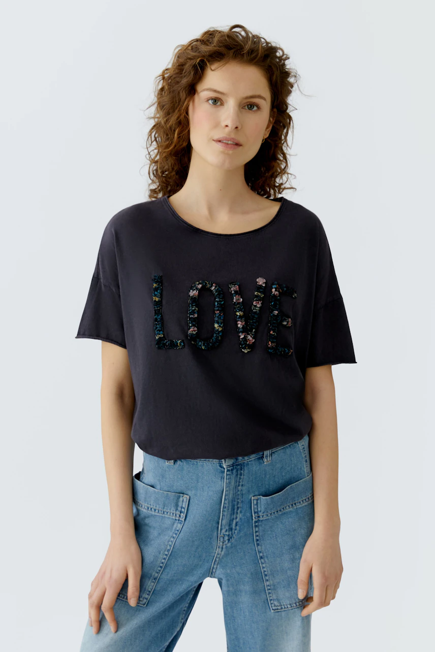 Casual women's T-shirt: Young woman in a dark tee with sequined 'LOVE' lettering and relaxed fit.