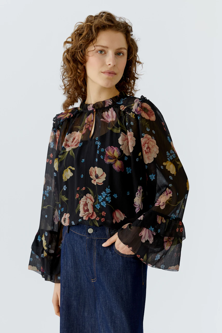 Floral blouse: Woman in a black sheer blouse with colorful flowers and flared sleeves, paired with a denim skirt.
