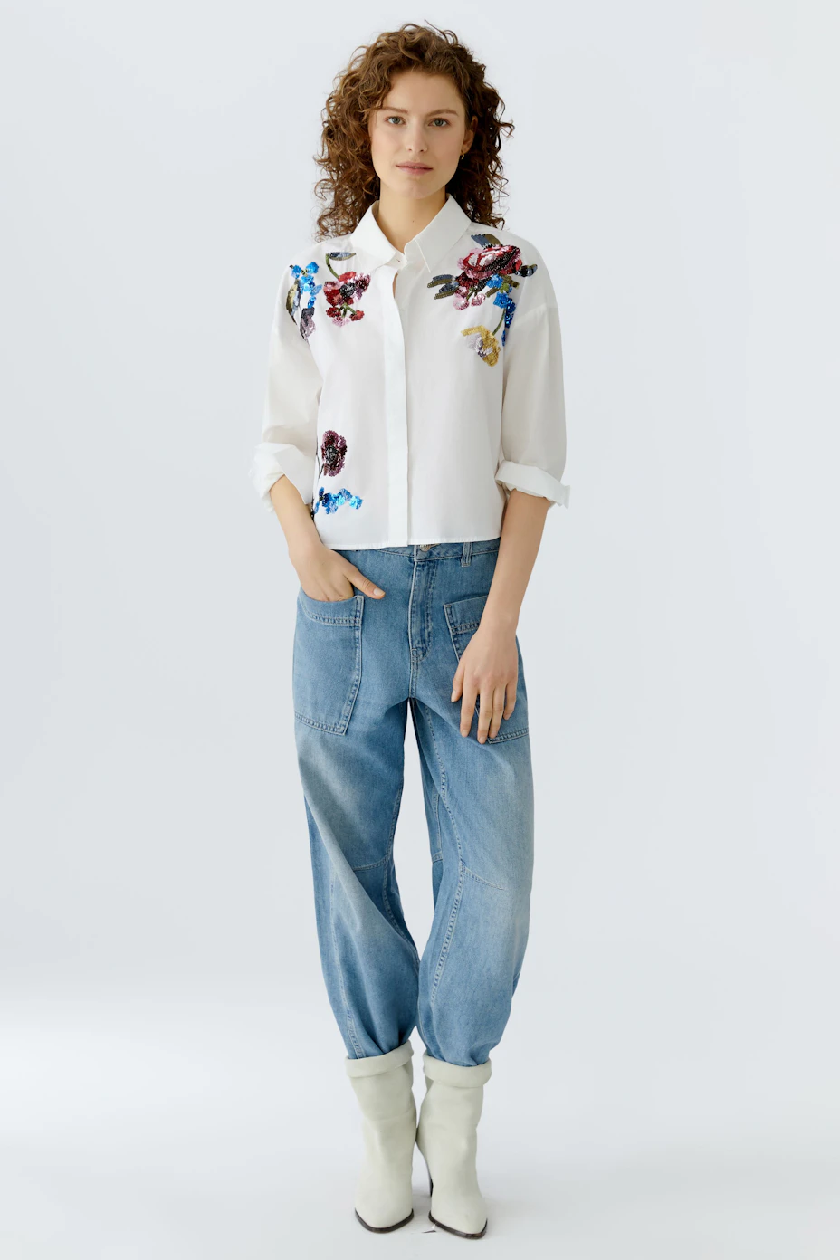 Cropped blouse: A woman in a white shirt with colorful floral embroidery, showcasing a casual style.