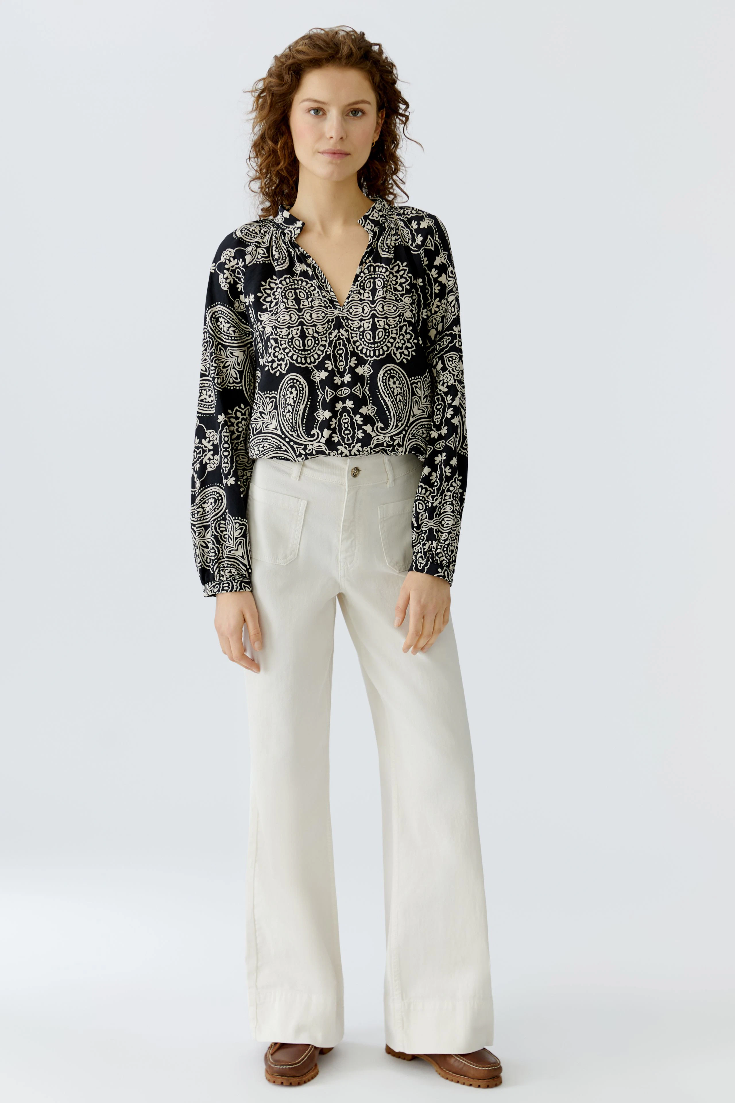 Damen-Bluse: Frau in schwarzer Bluse mit Paisleymuster und hellen, weiten Hosen.