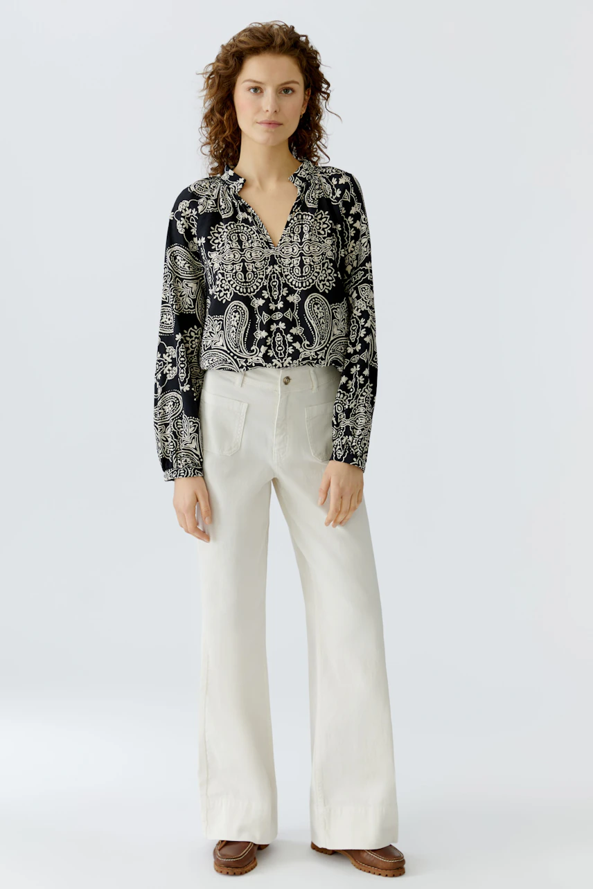 Stylish women's blouse: A woman in a black and white patterned blouse paired with light trousers.