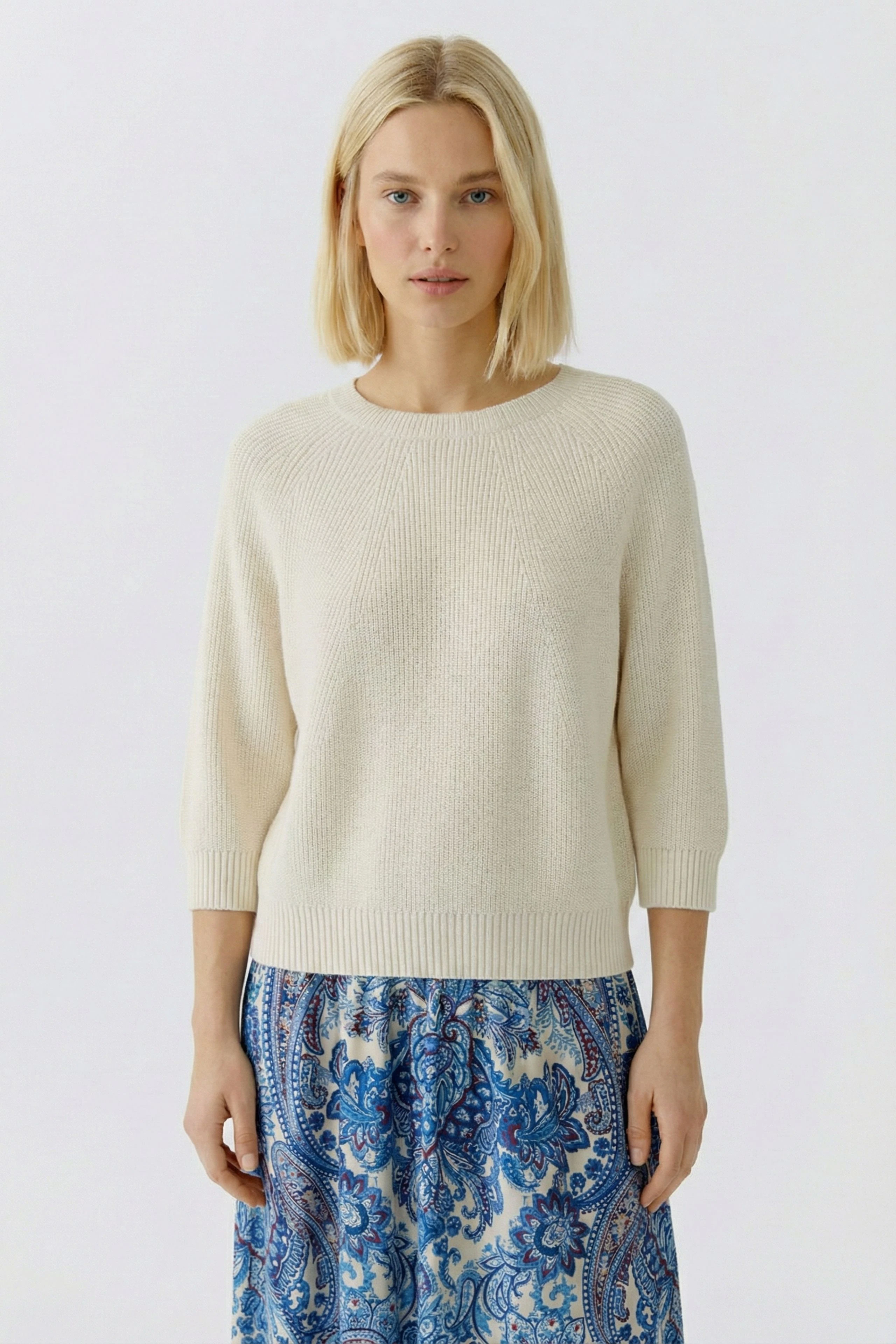 Casual women's pullover: Young woman in a cream pullover paired with a colorful patterned skirt.