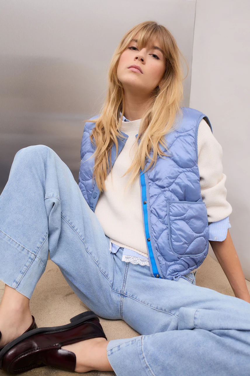 Casual women's pullover: Young woman in a light pullover, paired with a blue vest and relaxed jeans.