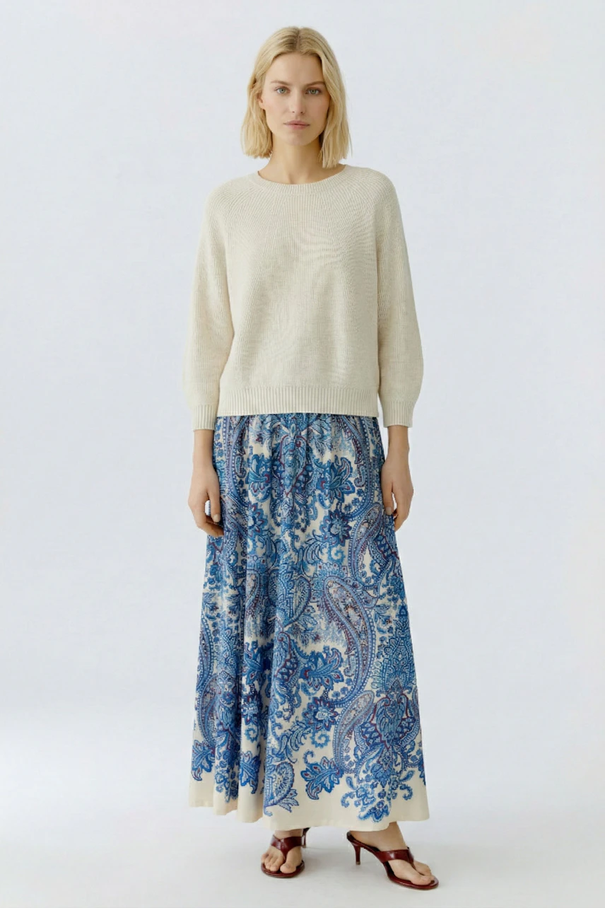 Casual women's pullover: A woman in a cream pullover paired with a blue patterned skirt stands confidently.