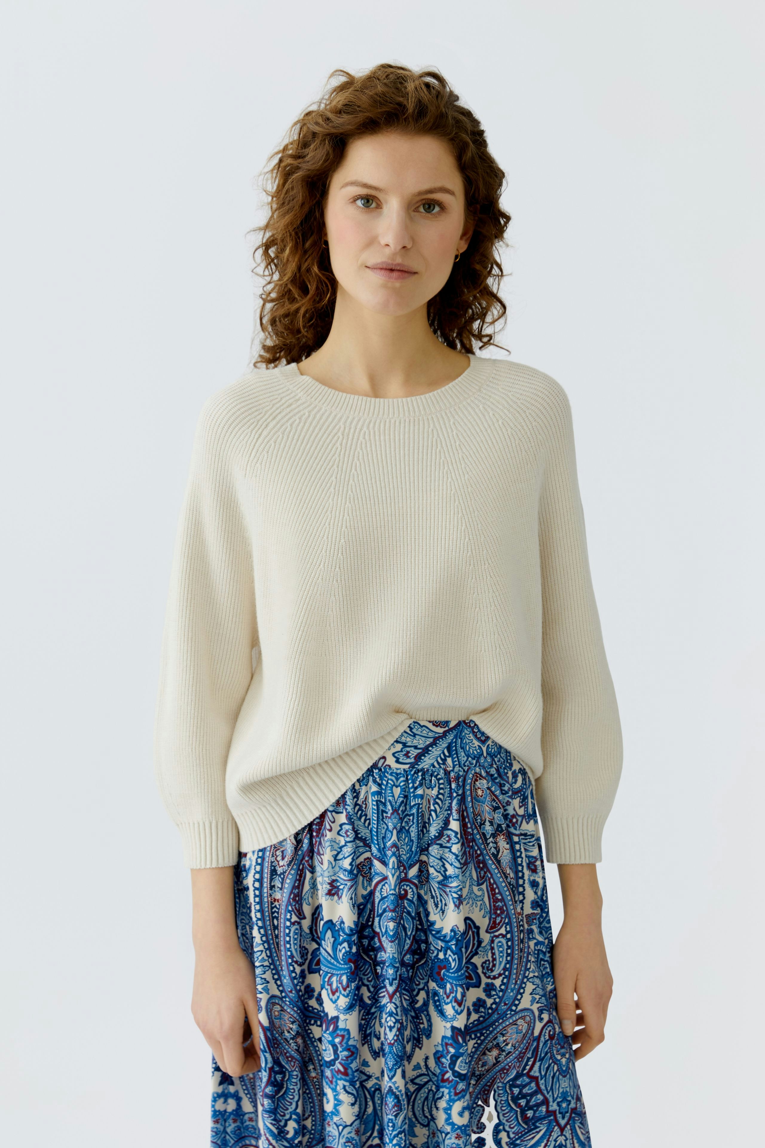 Damen-Pullover: Frau trägt einen beigen, lässigen Pullover mit 3/4-Ärmeln und kombiniert ihn mit einem bunten Rock.