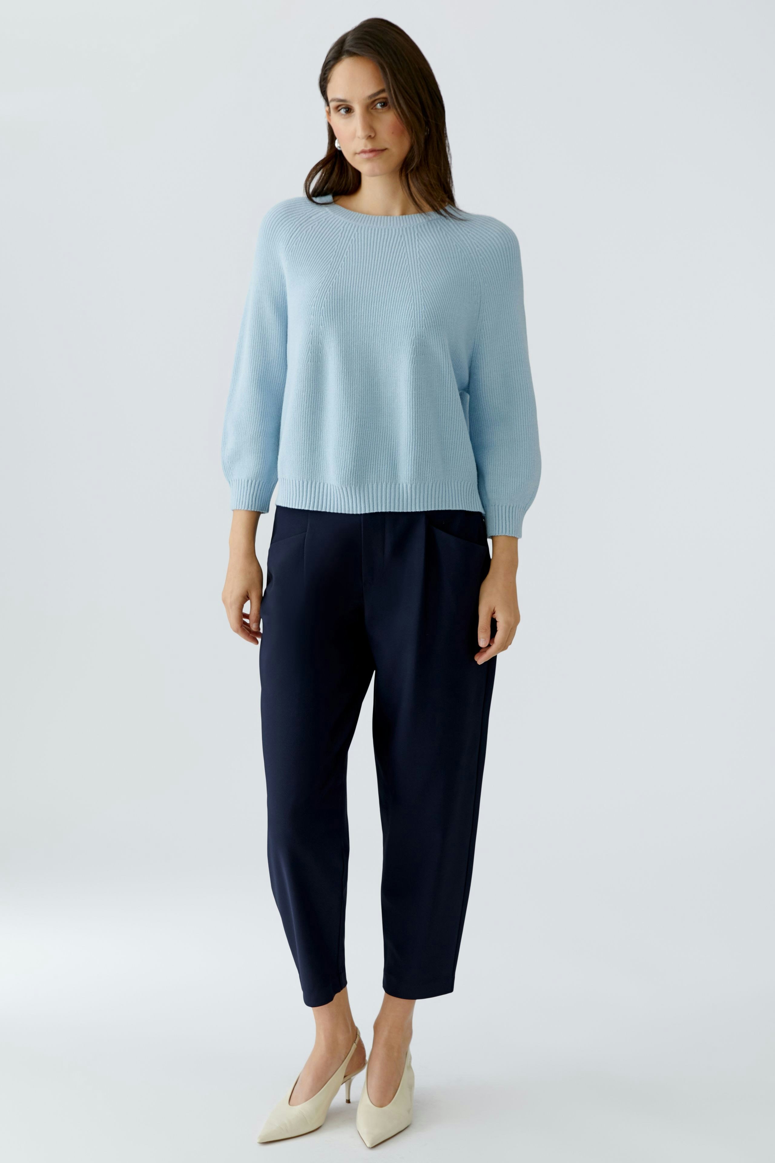 Damen-Pullover: Junge Frau in hellblauem Pullover mit lässigen Hosen steht entspannt.