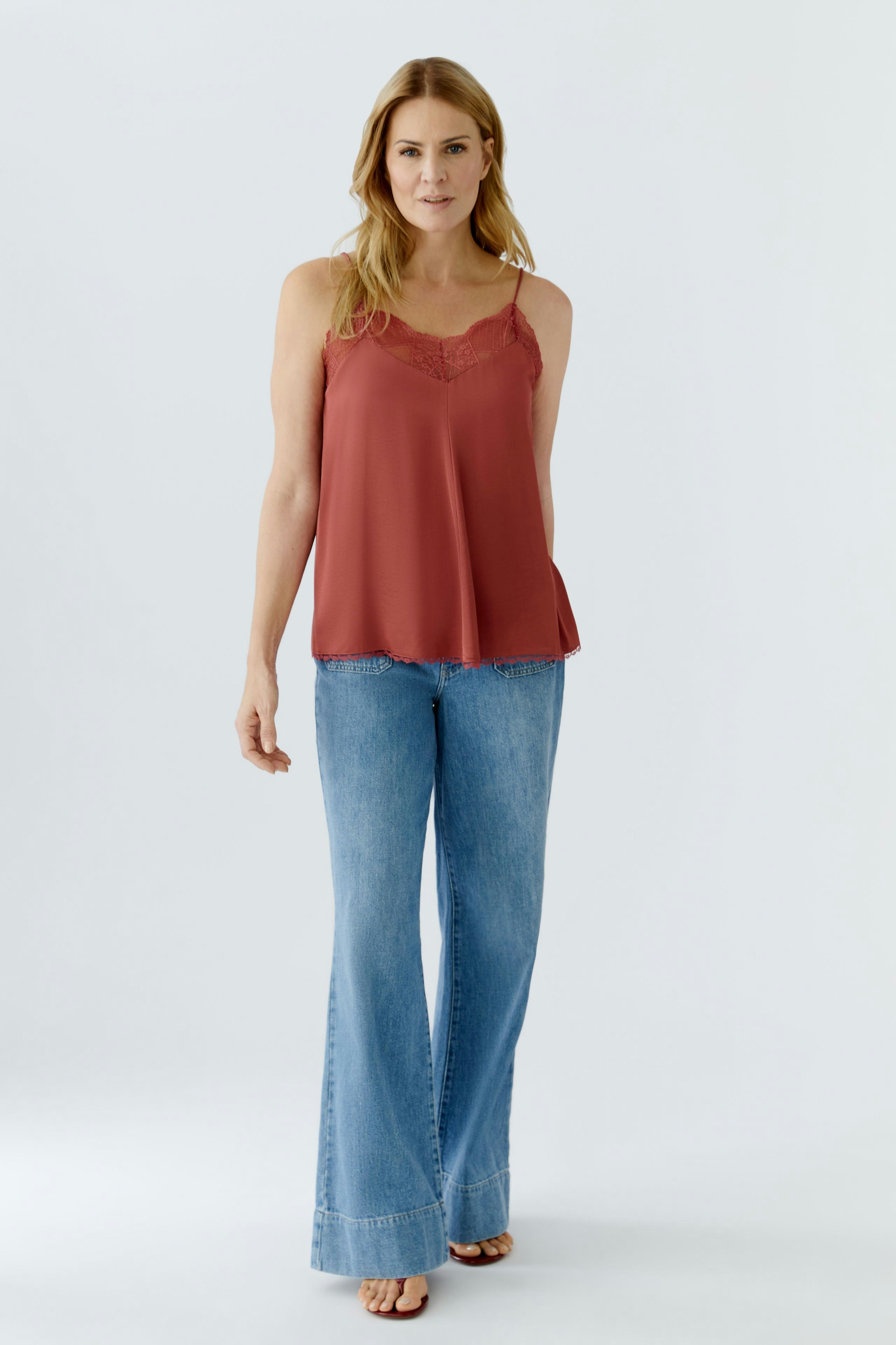 Lässiges Damen-Top: Frau trägt ein rotes Spaghetti-Top mit Spitzenbesatz und weiten Jeans.