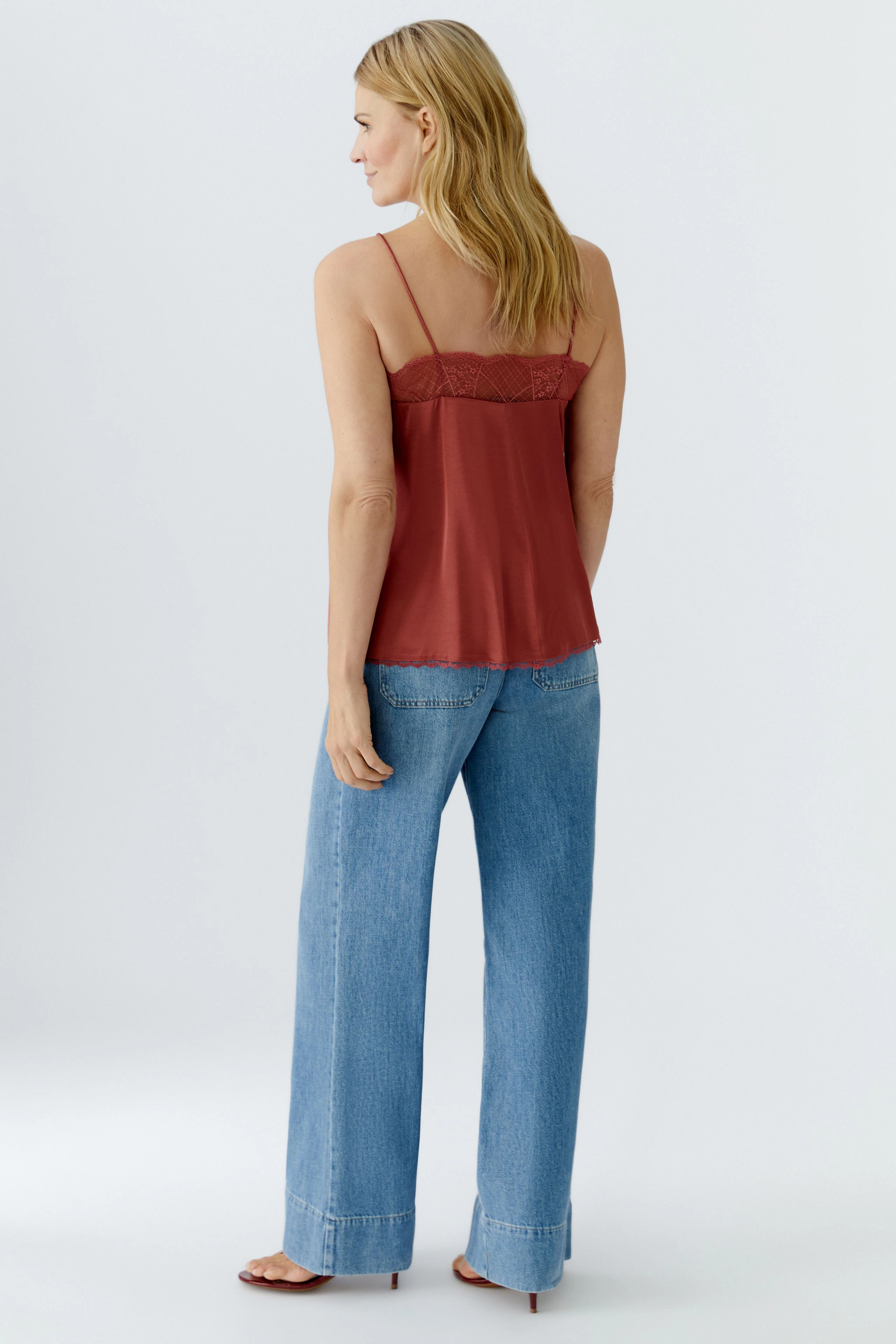 Damen-Top: Frau trägt ein rotes Spaghettiträgertop mit Spitzenbesatz und lässigen Jeans.