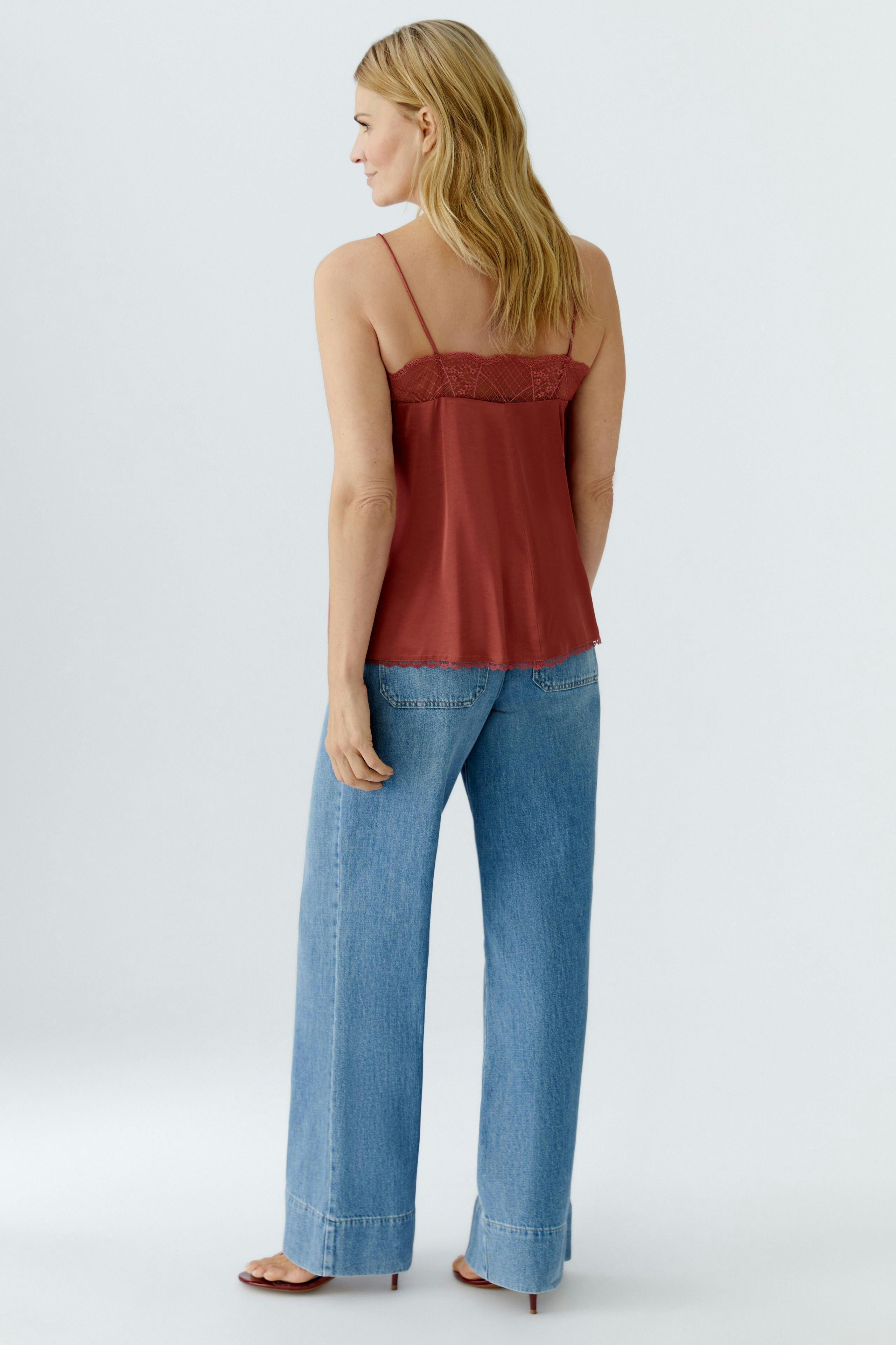 Damen-Top: Frau trägt ein rotes Spaghettiträgertop mit Spitzenbesatz und lässigen Jeans.