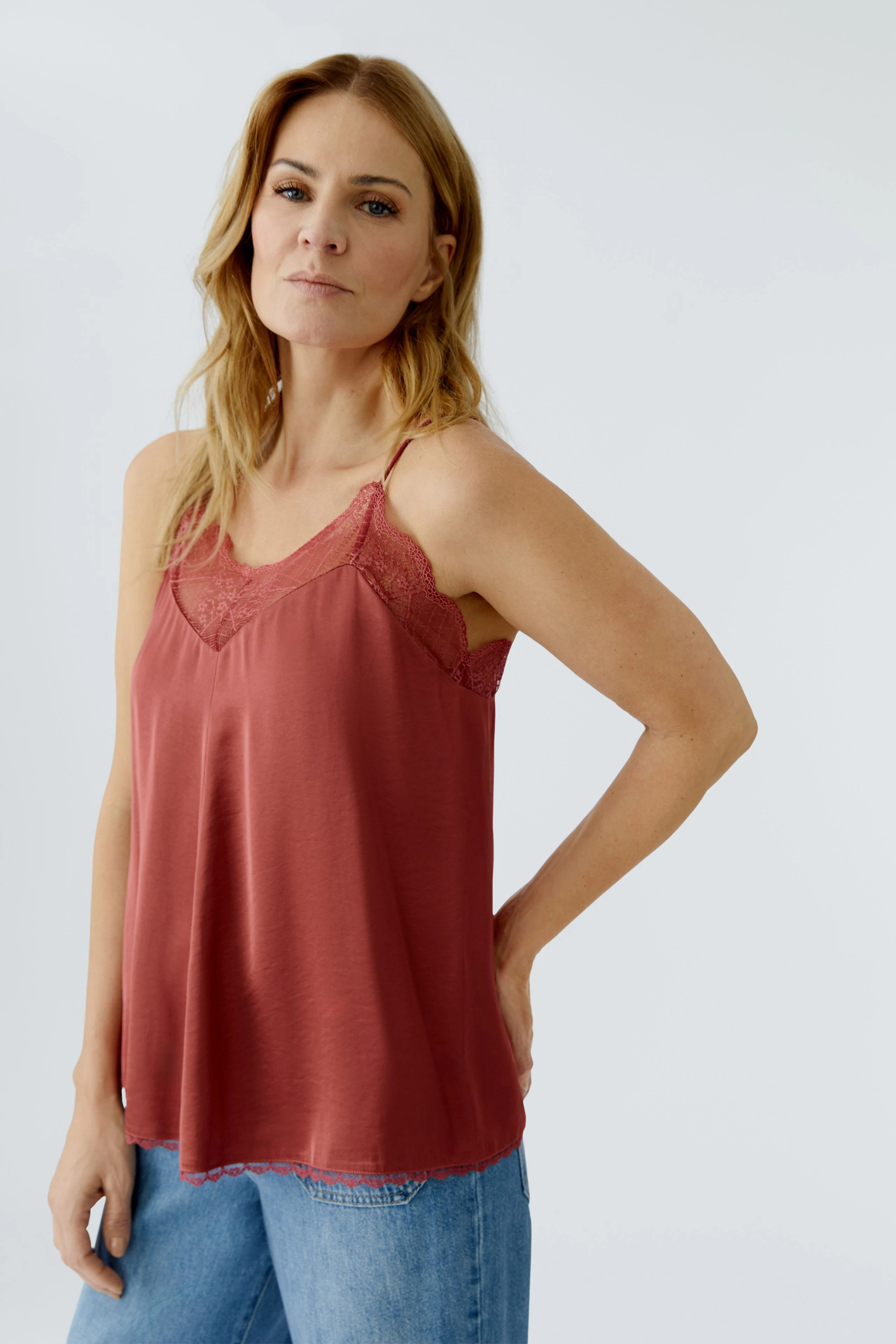 Bequeme Damen-Top: Frau trägt ein rotes Spaghetti-Top mit Spitzenakzenten und lässigen Jeans.