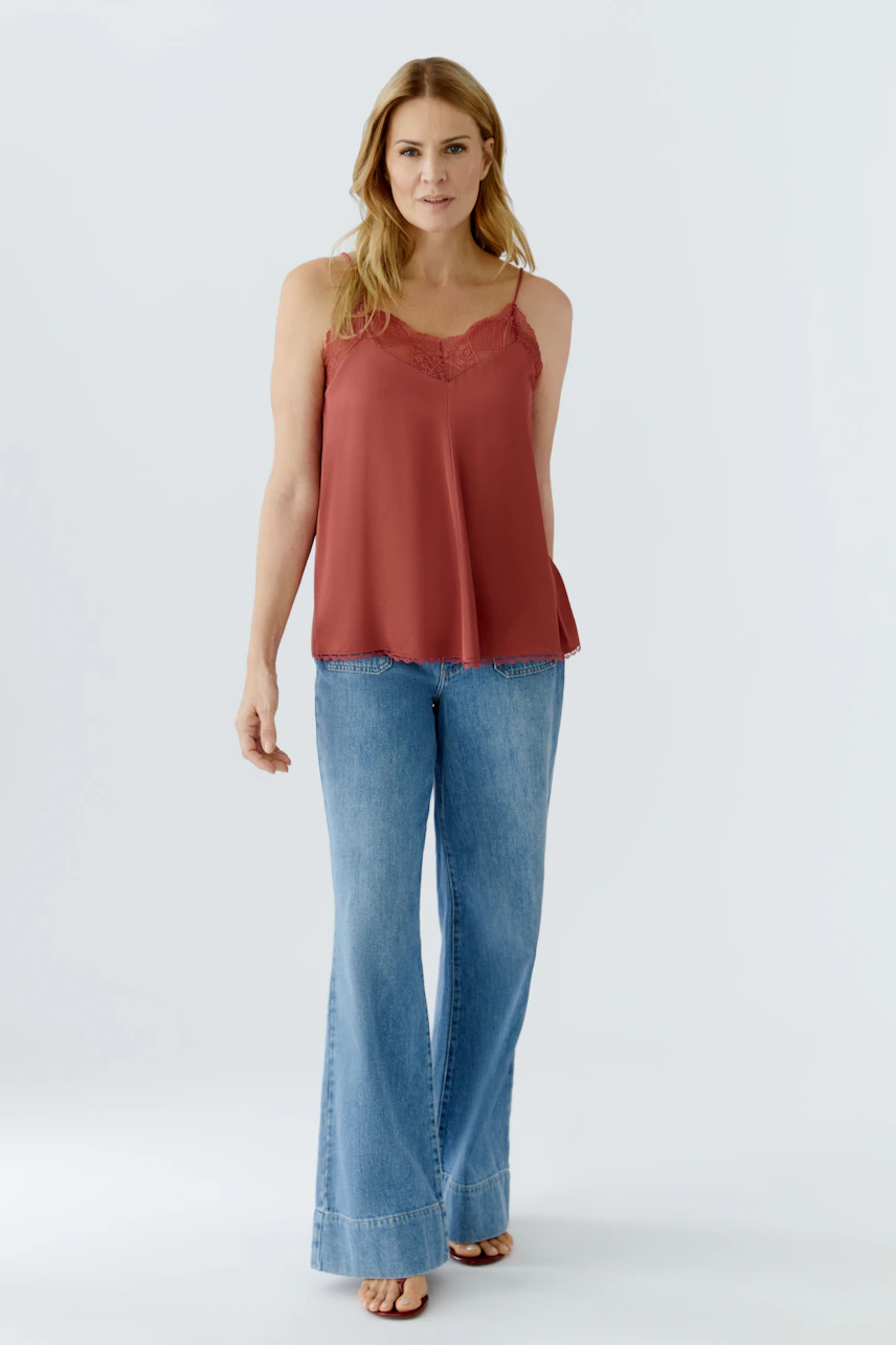Lässiges Damen-Top: Frau trägt ein rotes Spaghetti-Top mit Spitzenbesatz und weiten Jeans.