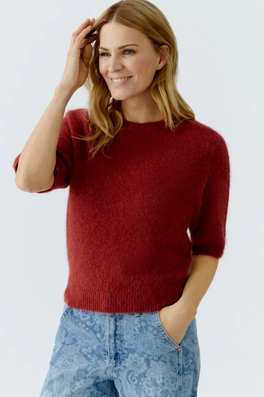 Damen-Pullover: Frau in rotem, weichem Strickpullover mit kurzen Ärmeln und lässigen Jeans.