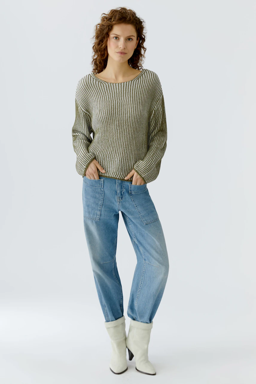 Damen-Pullover: Frau in gestreiftem Pullover mit lockeren Jeans und weißen Stiefeln steht entspannt.