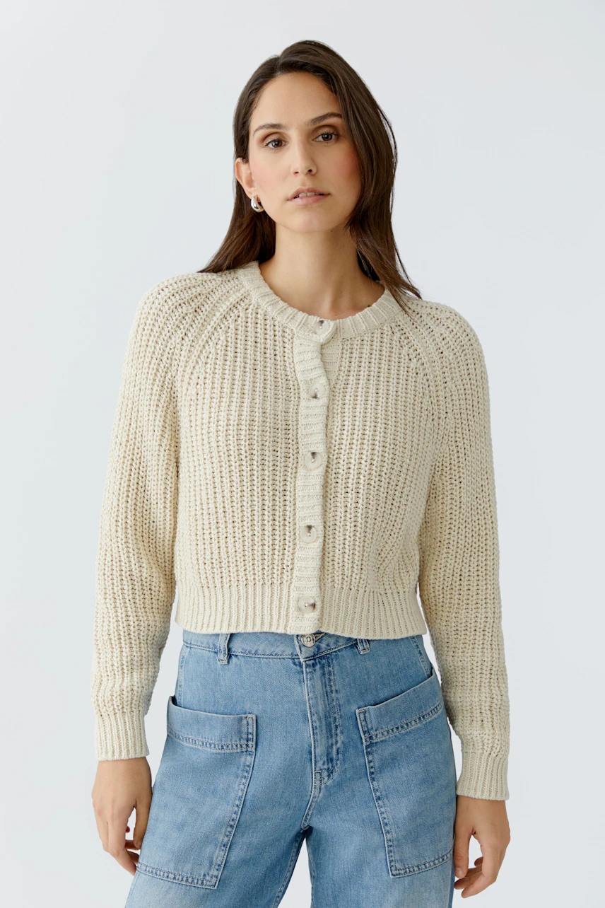 Casual women's cardigan: A woman in a cream knitted cardigan with buttons and relaxed fit jeans.