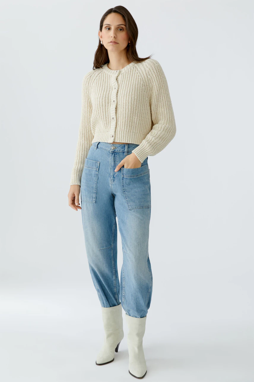 Casual women's cardigan: A woman in a cream-colored knitted cardigan with buttons and relaxed-fit jeans.