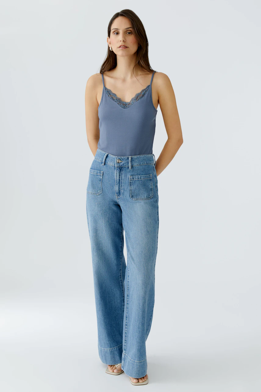 Casual women's top: A woman in a blue lace-trimmed tank top paired with wide-leg jeans.