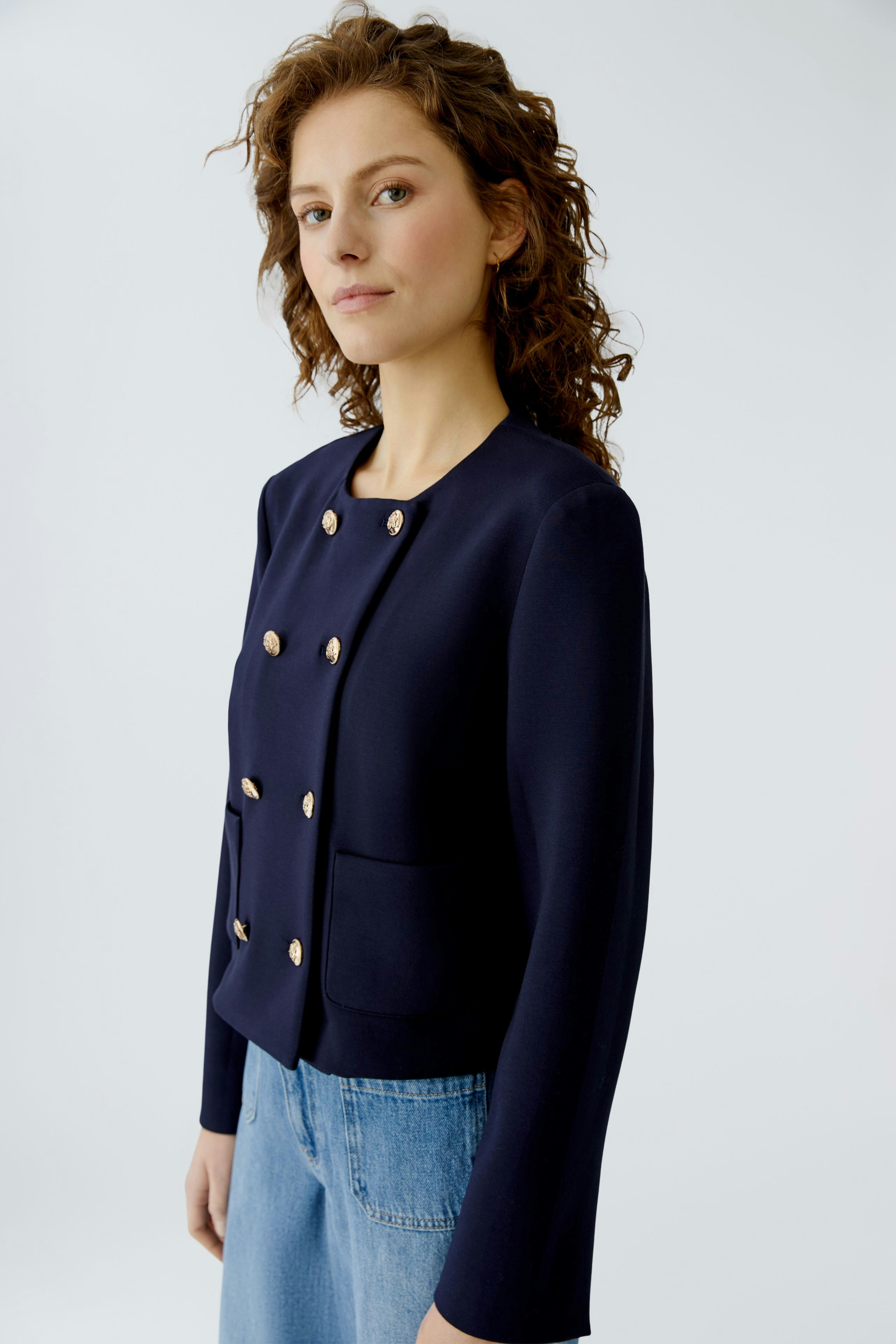 Casual women's jacket: A woman in a navy jacket with gold buttons and pockets, paired with jeans.