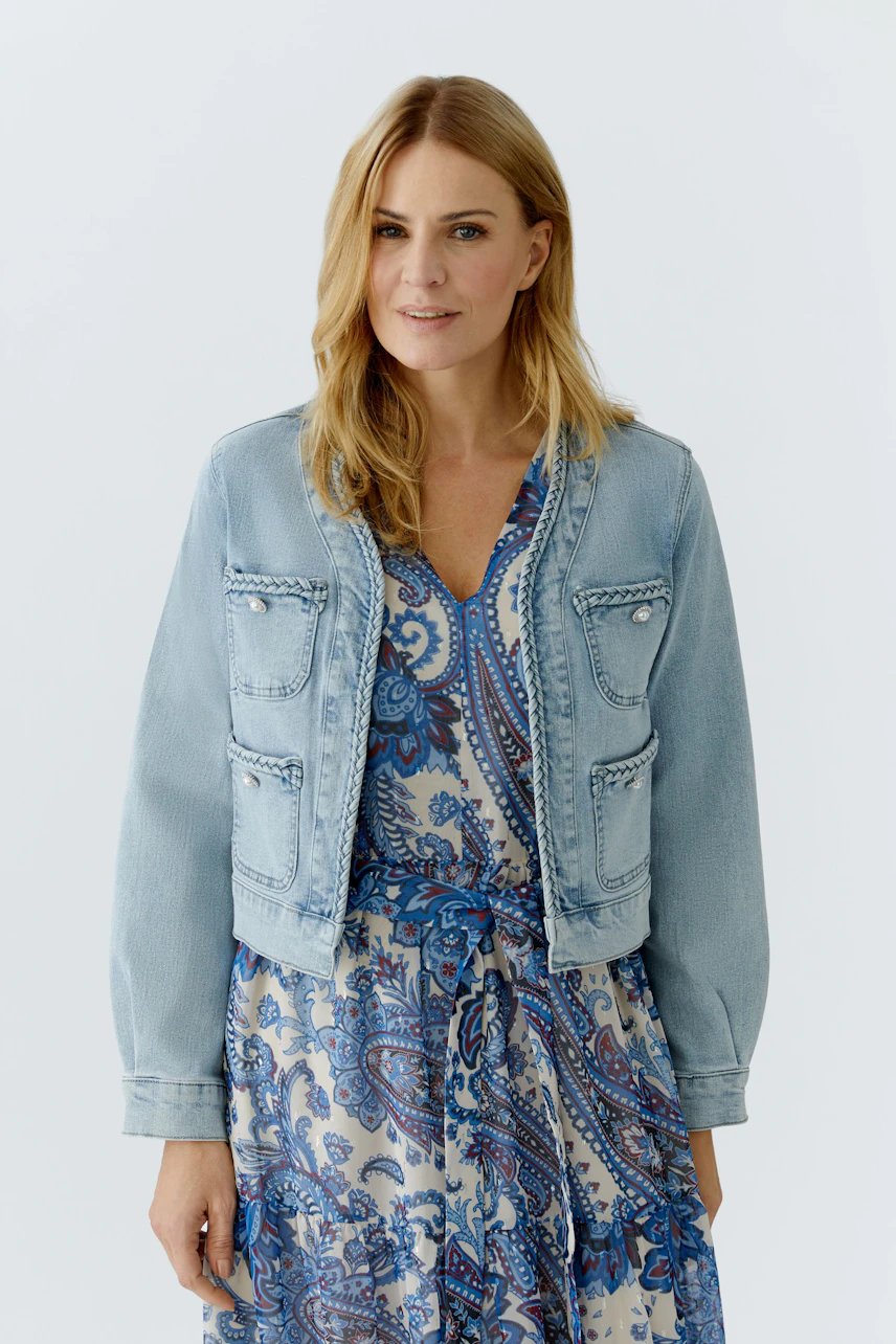 Damen-Jeansjacke: Frau in heller Jeansjacke über einem gemusterten Kleid, lässiger Look.