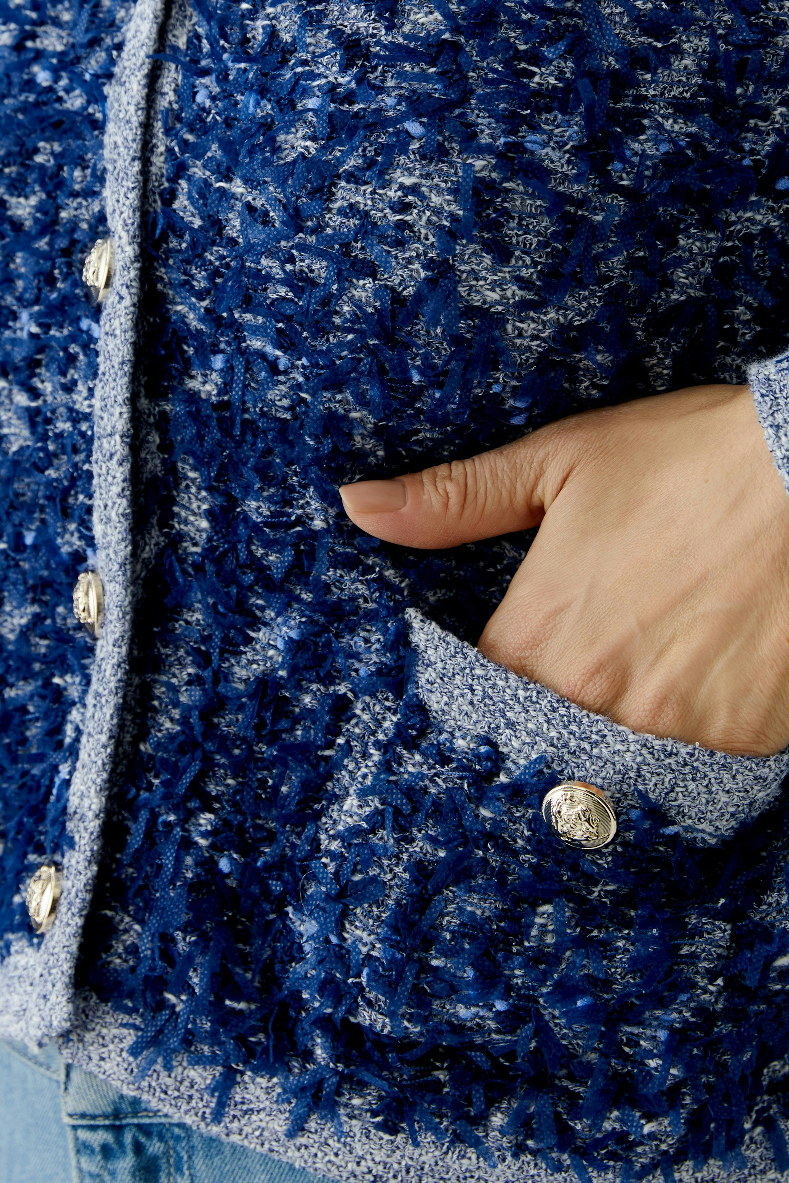 Casual women's cardigan: Close-up of a woman’s hand in a blue textured cardigan with pockets.