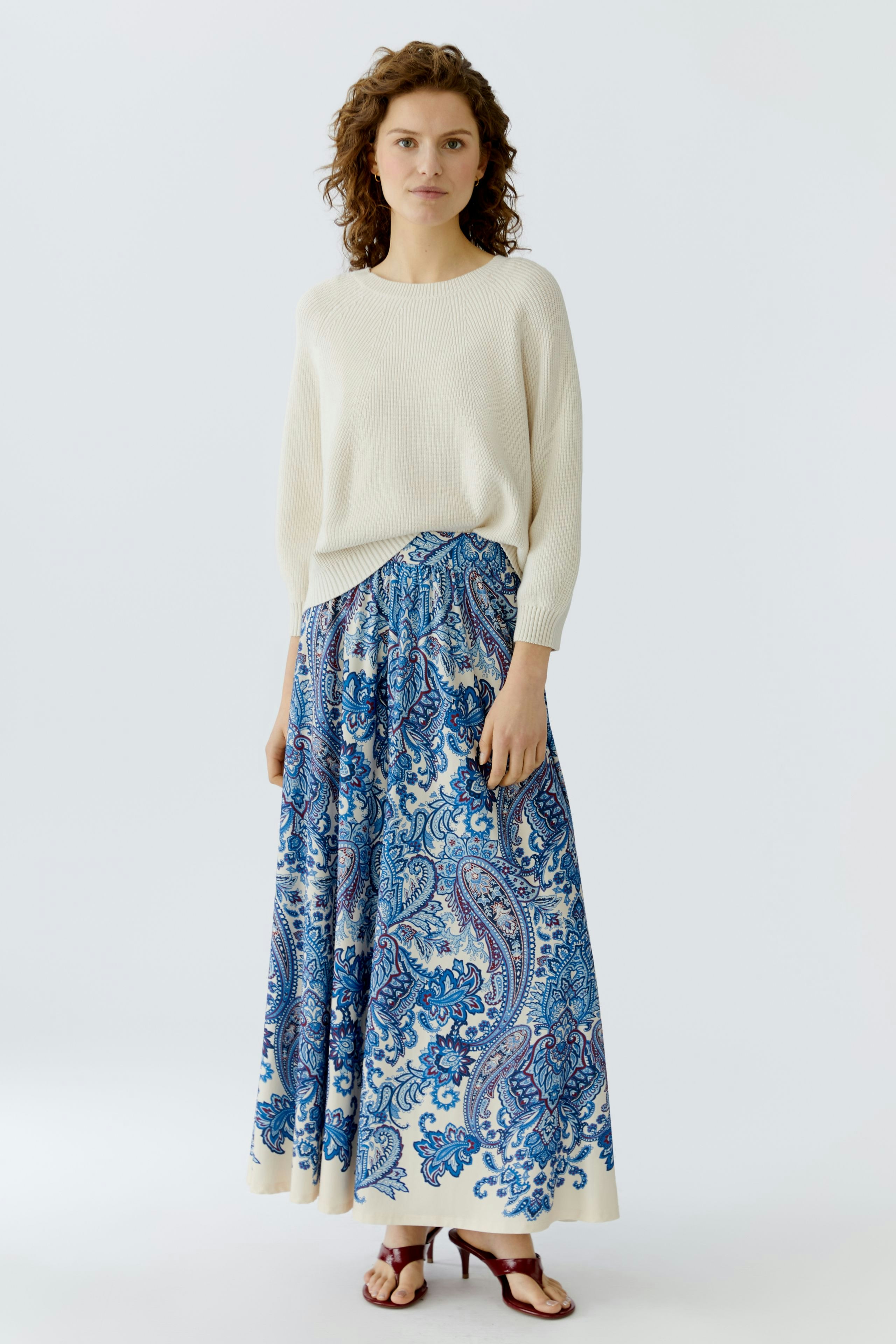 A-line skirt: Woman in a casual outfit with a patterned skirt and light pullover, standing confidently.