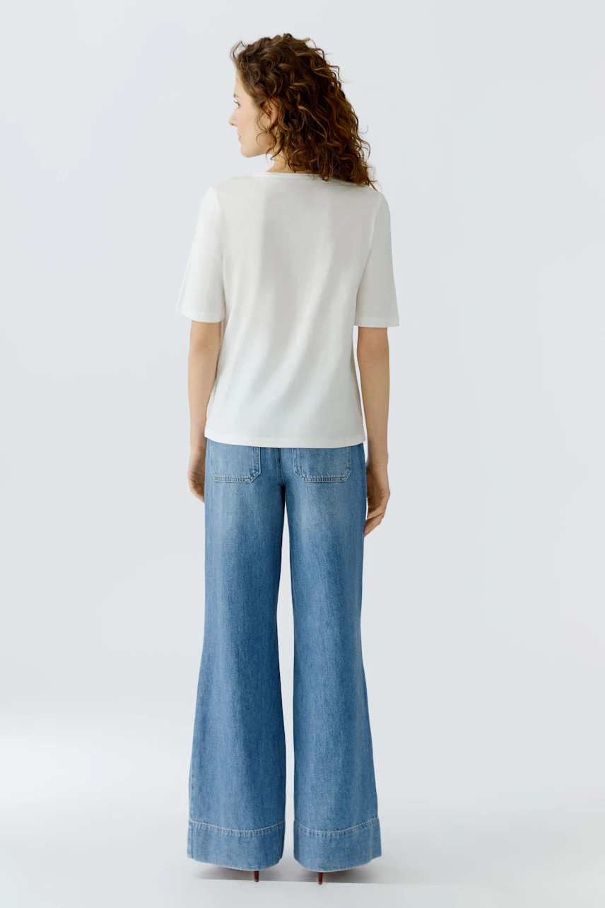 Casual women's T-shirt: A woman in a white short-sleeve top paired with wide-leg jeans.