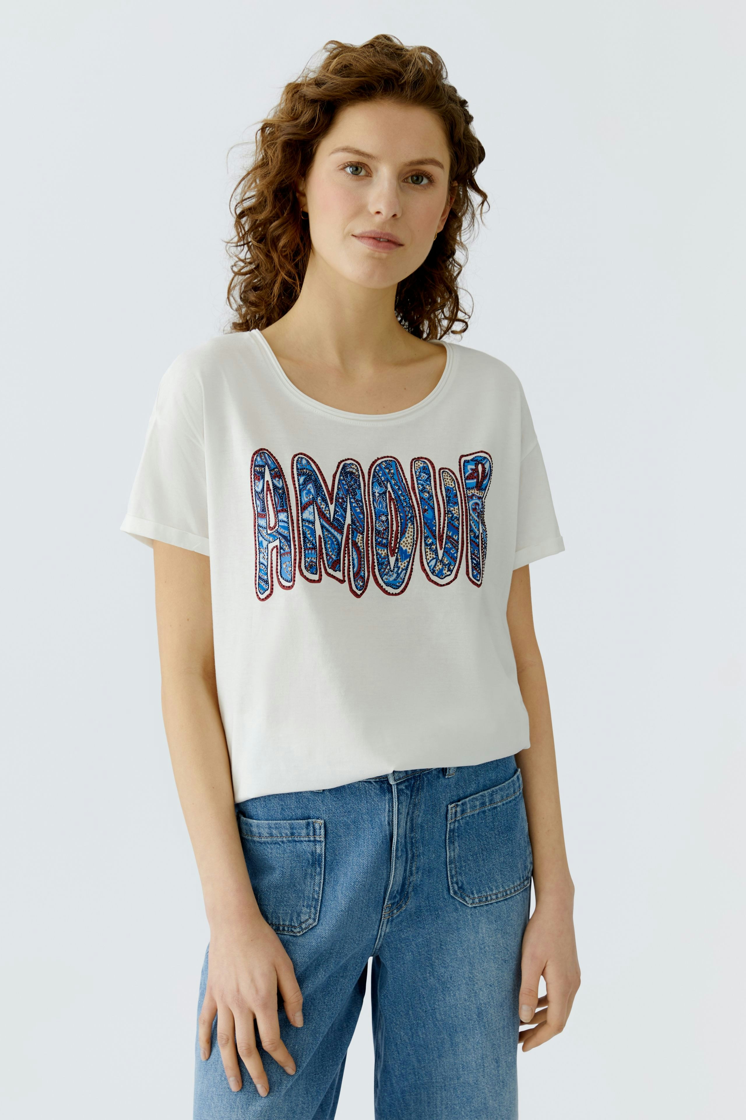 Casual women's T-shirt: Young woman in a white tee with 'AMOUR' print, paired with blue jeans.