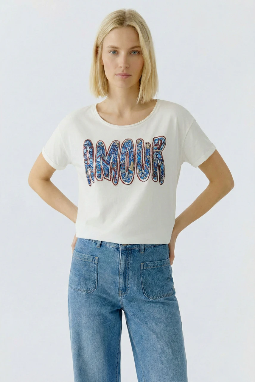 Casual women's T-shirt: Young woman in a white tee with colorful 'Amour' print, paired with denim.