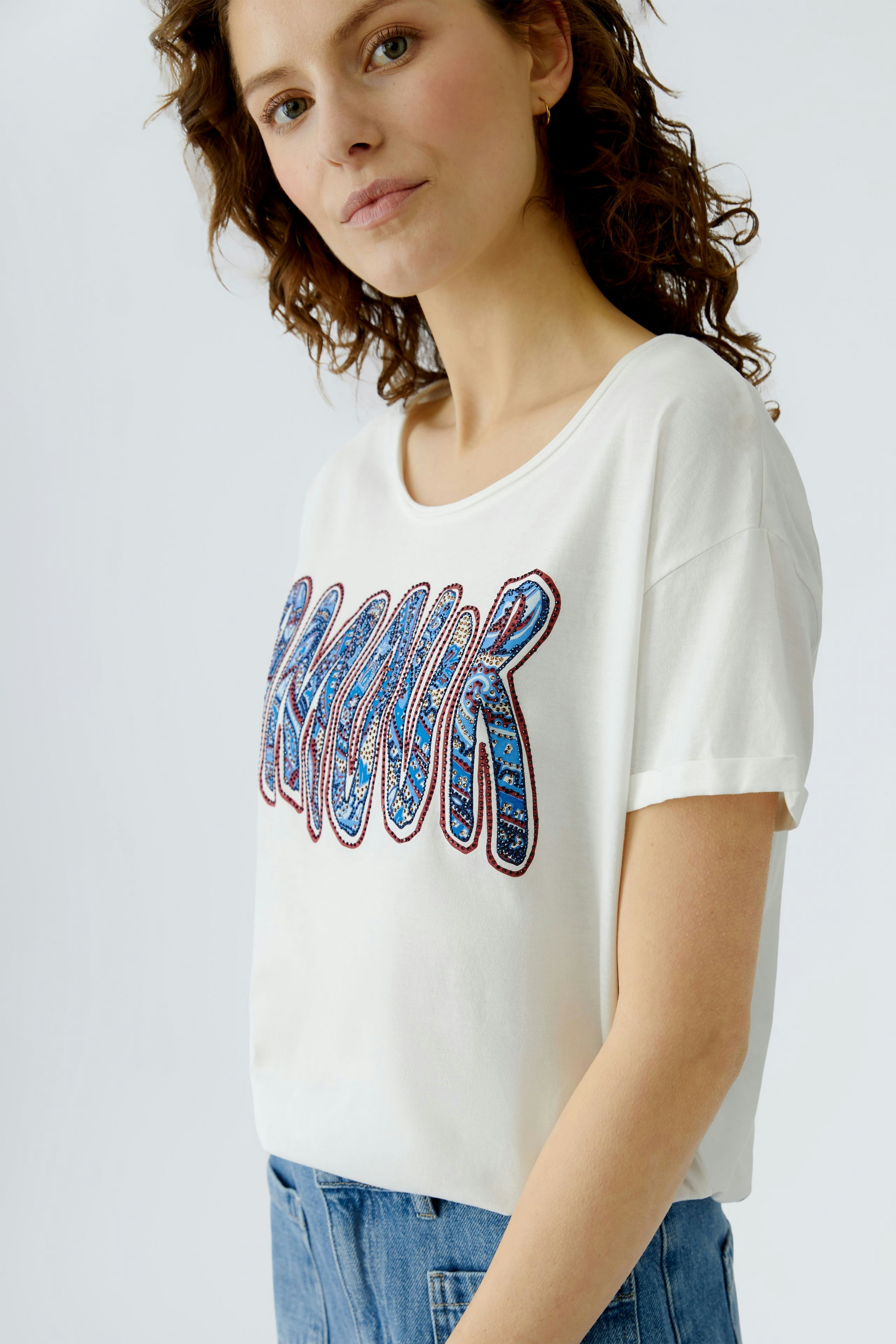 Casual women's T-shirt: Young woman in a white tee with colorful 'Amour' print, paired with denim.