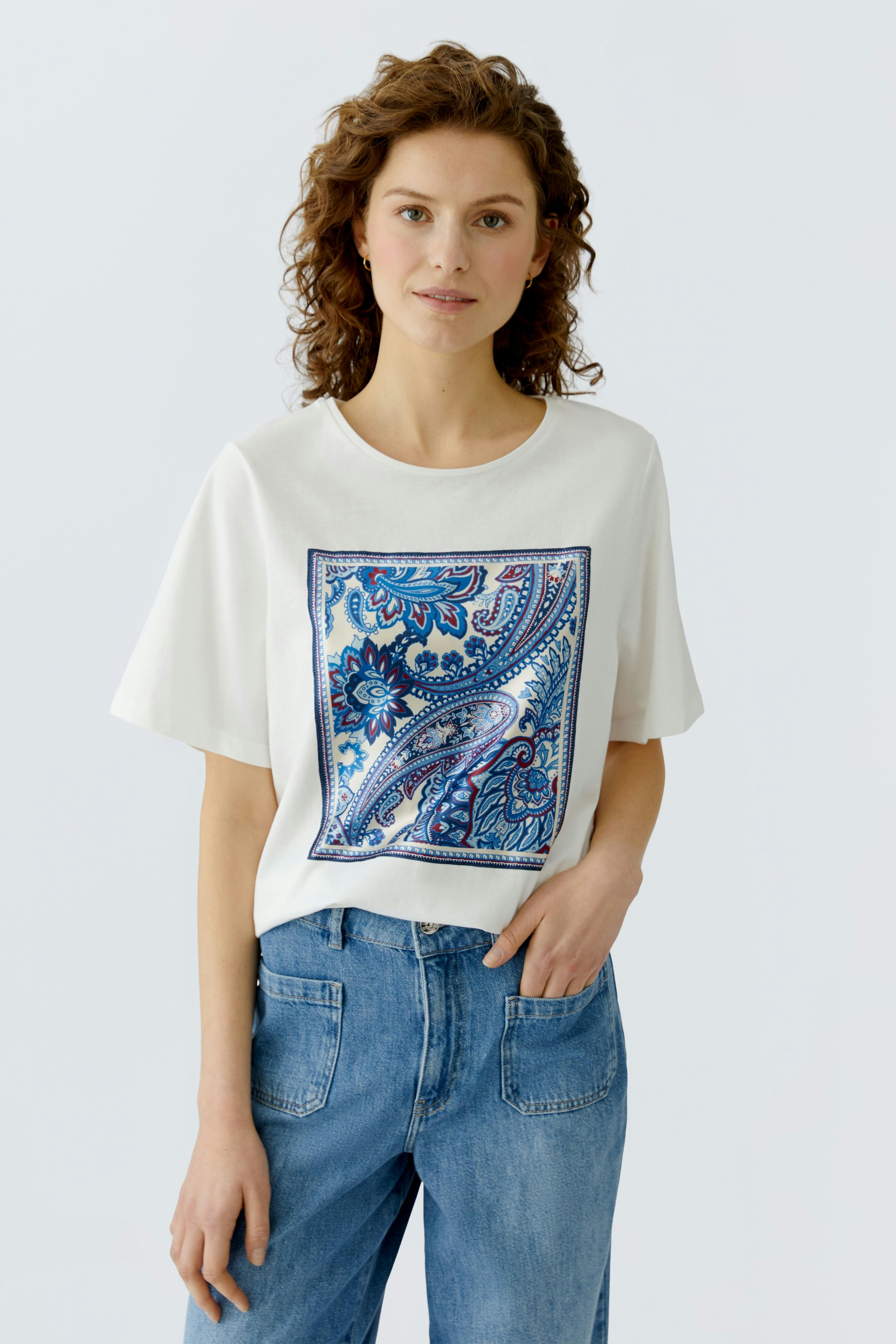 Casual women's T-shirt: Young woman in a white tee with a colorful paisley print, paired with blue jeans.