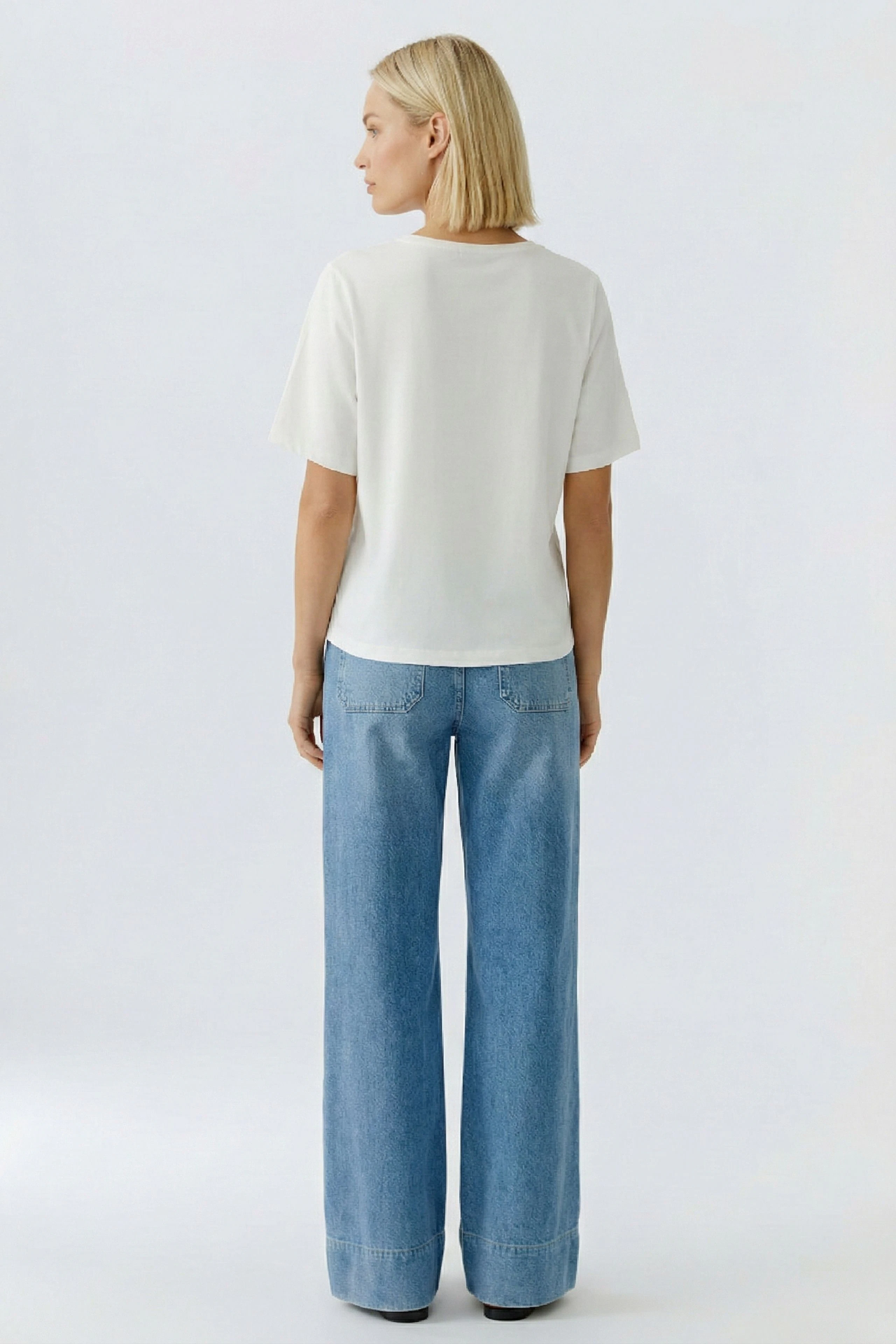 Luftiges Damen-T-Shirt: Frau mit lockigen Haaren trägt ein weißes T-Shirt und weite Jeans.