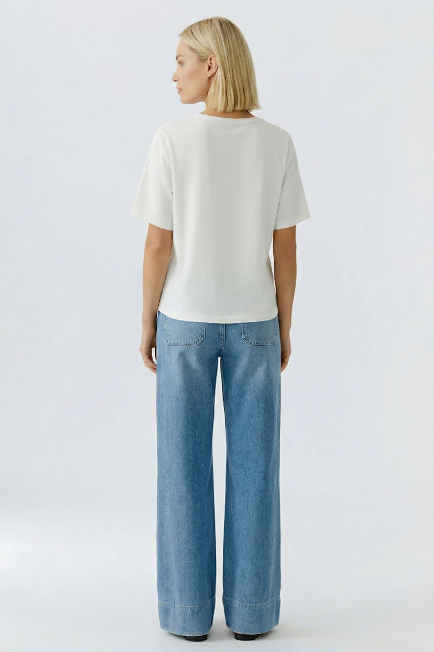 Luftiges Damen-T-Shirt: Frau mit lockigen Haaren trägt ein weißes T-Shirt und weite Jeans.