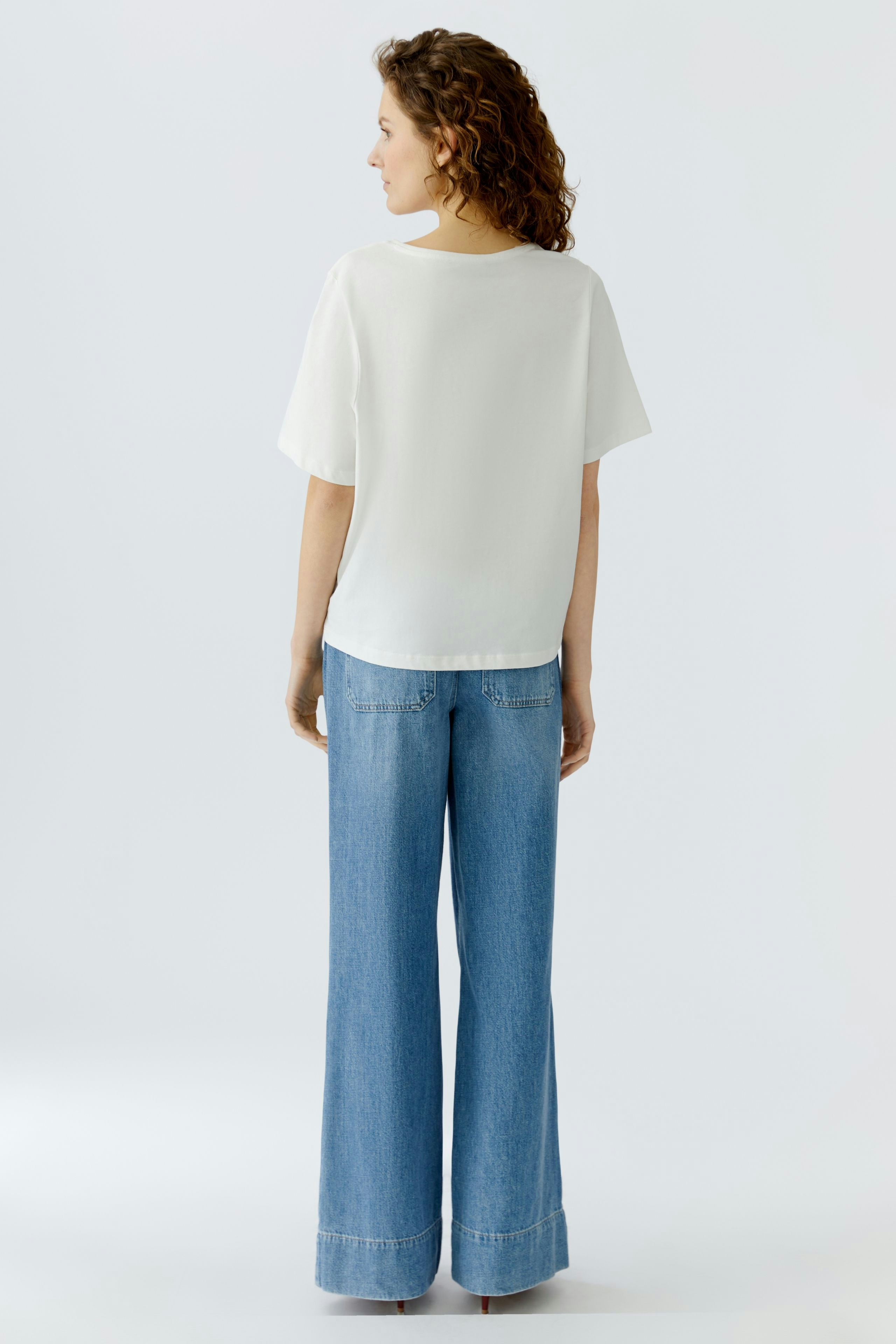 Casual women's T-shirt: A woman in a white top paired with wide-leg jeans, showcasing a relaxed style.