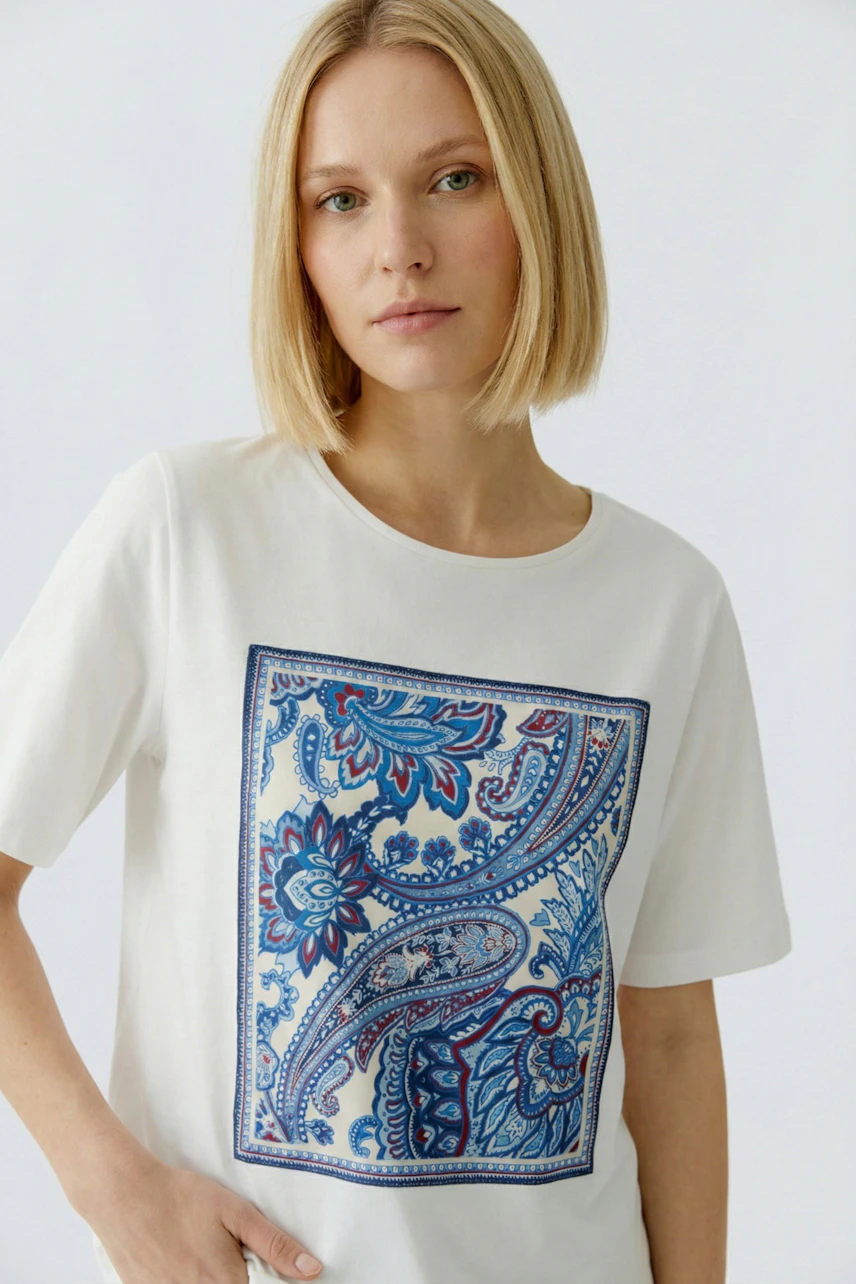 Damen-T-Shirt: Junge Frau trägt ein weißes T-Shirt mit buntem Paisleymuster auf der Vorderseite.