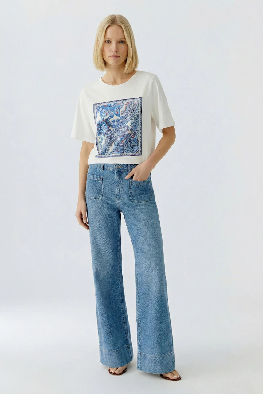 Damen-T-Shirt: Junge Frau trägt ein weißes T-Shirt mit buntem Druck und lässigen Jeans.